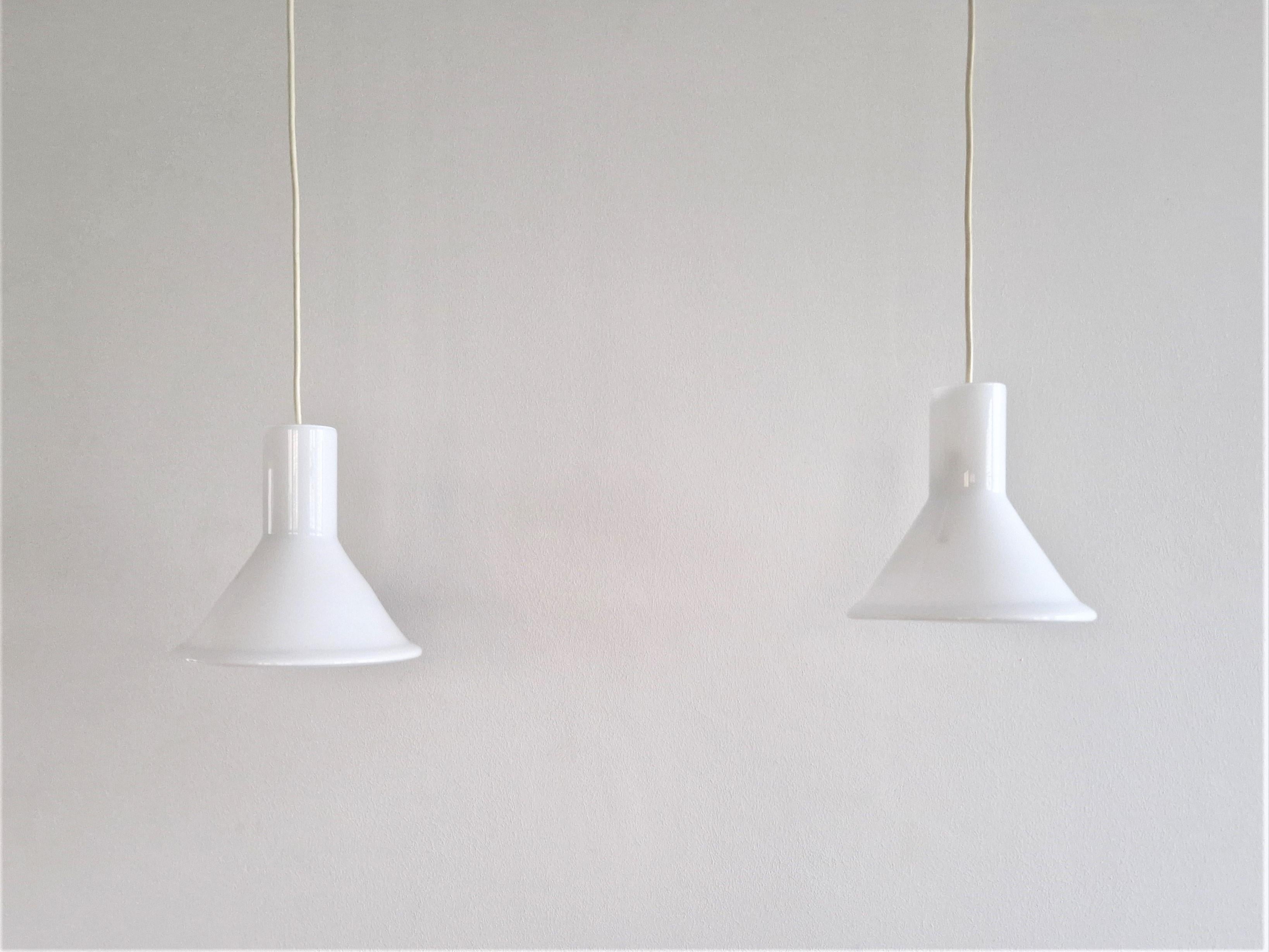 This set of 2 'Mini P&T' pendant lamps was designed by Michael Bang for Holmegaard in the 1970s. The Danish design lamp is made of white opaline glass. When lit, it gives a beautiful soft white light. These lamps are marked at the inside by