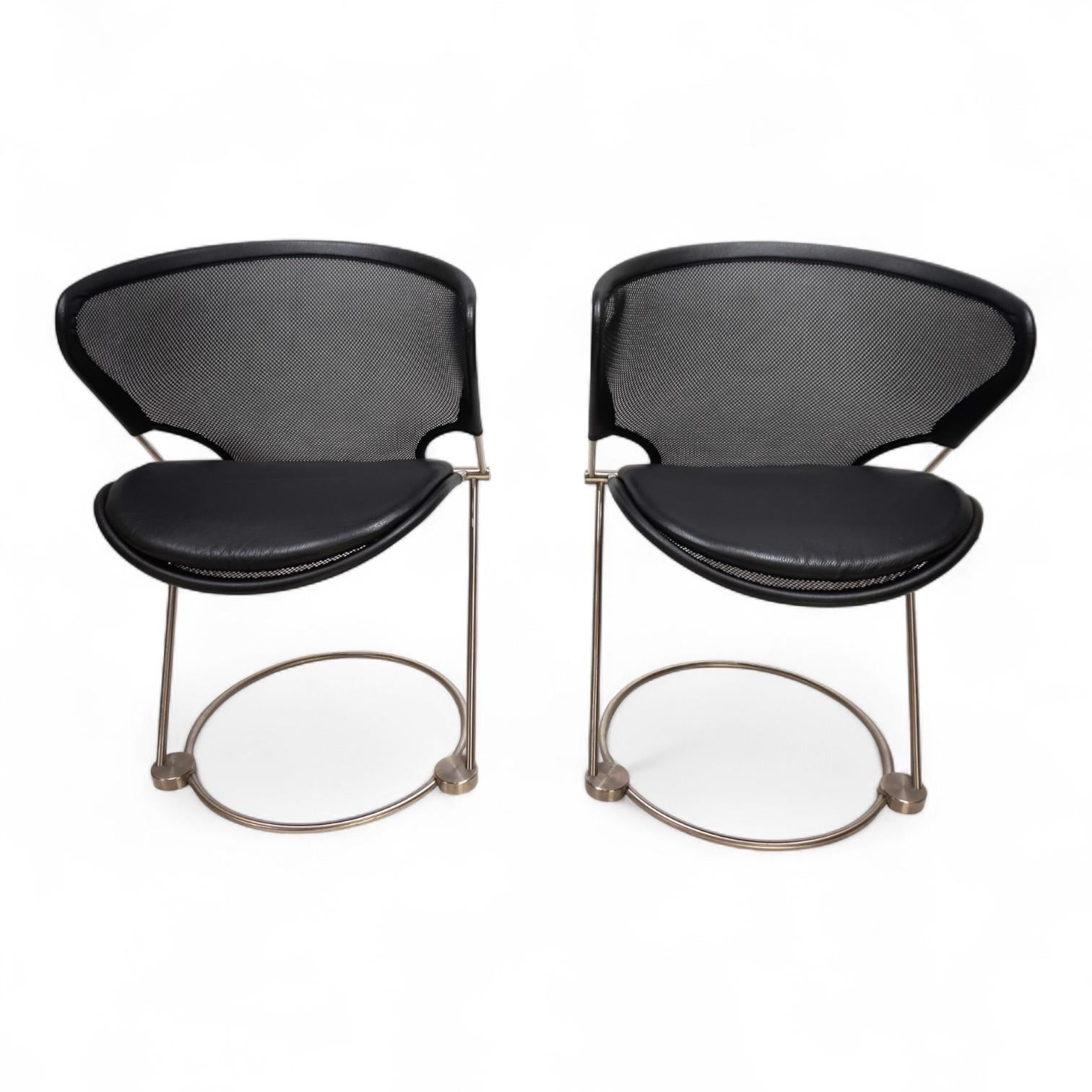 Le due sedie Nuvola sono in condizioni eccellenti, come nuove. La solida struttura in acciaio inox si armonizza perfettamente con la rete in poliestere nero ben tesa delle sedute e degli schienali. La rete è bordata da cinghie di pelle nera agli