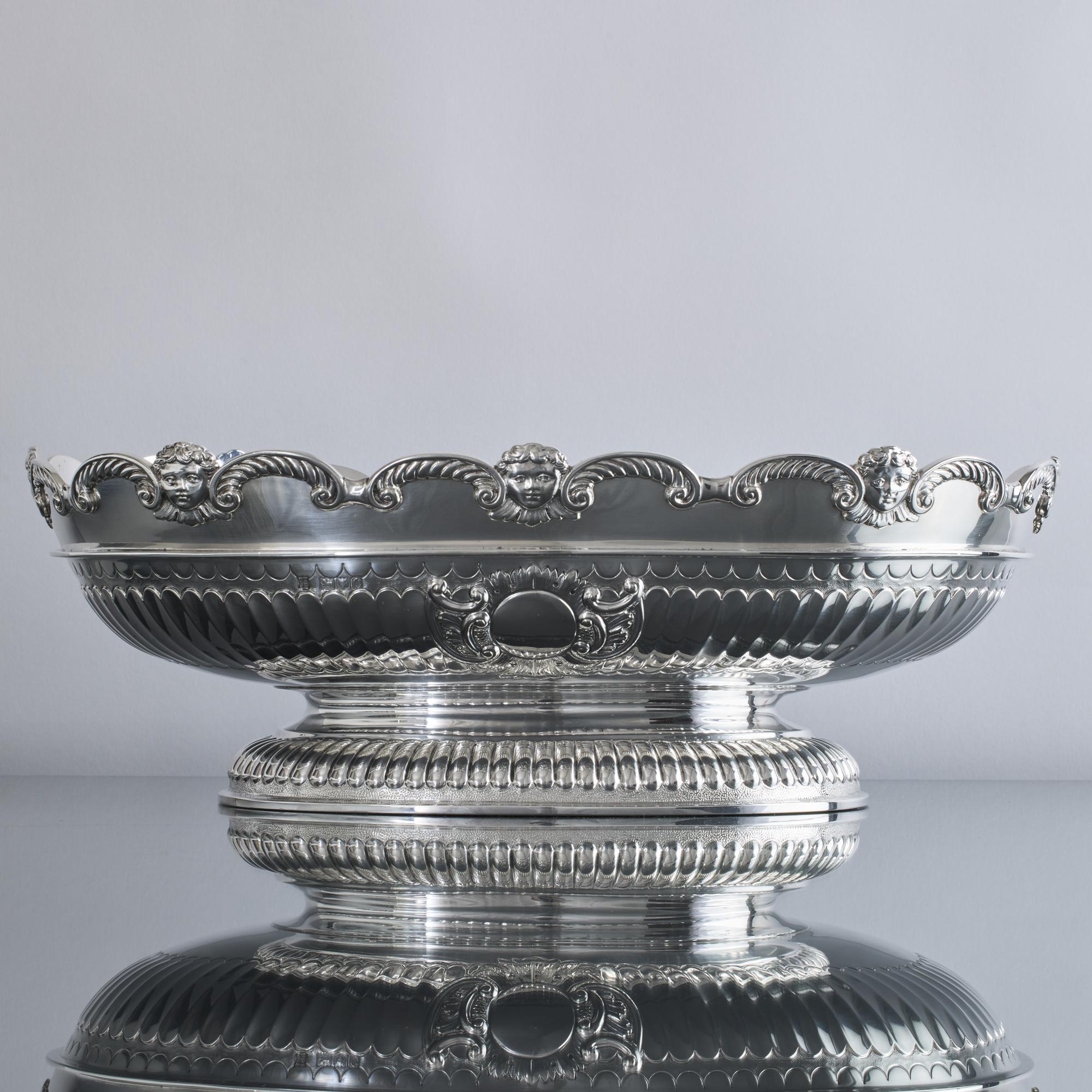 Superior quality oval-shaped silver fruit bowl, with a Monteith-style rim decorated with cast and applied scrolled gadroon patterns and cherub masks. The body and base are hand chased with fluting and a cartouche on either side. 
 
 This lovely bowl