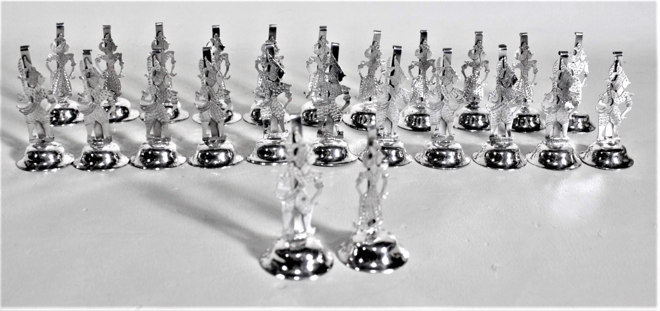 This set of twenty four silver plated place card or menu holders are unsigned, but presumed to have been made in Asia in approximately 1960 in a Tibetan style. The holders are composed of a stamped metal which has been silver plated and heavily