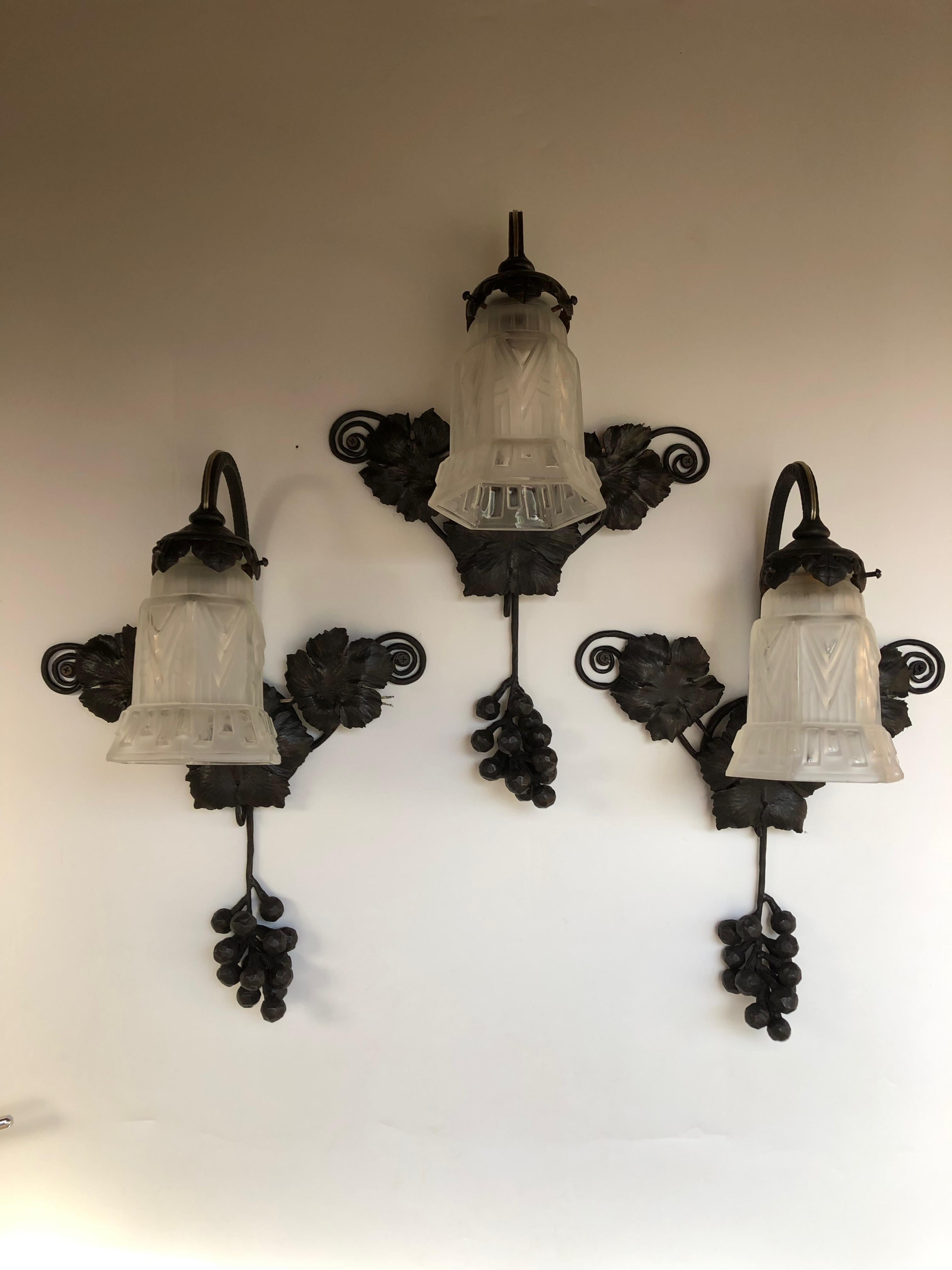 Suite of 3 art deco wall lights around 1930.
Wrought iron frame decorated with vine leaves and bunches of grapes.
Molded glass tulip with geometric decoration.
Wall lights  attributed to Hettier & Vincent.
In perfect state of conservation and