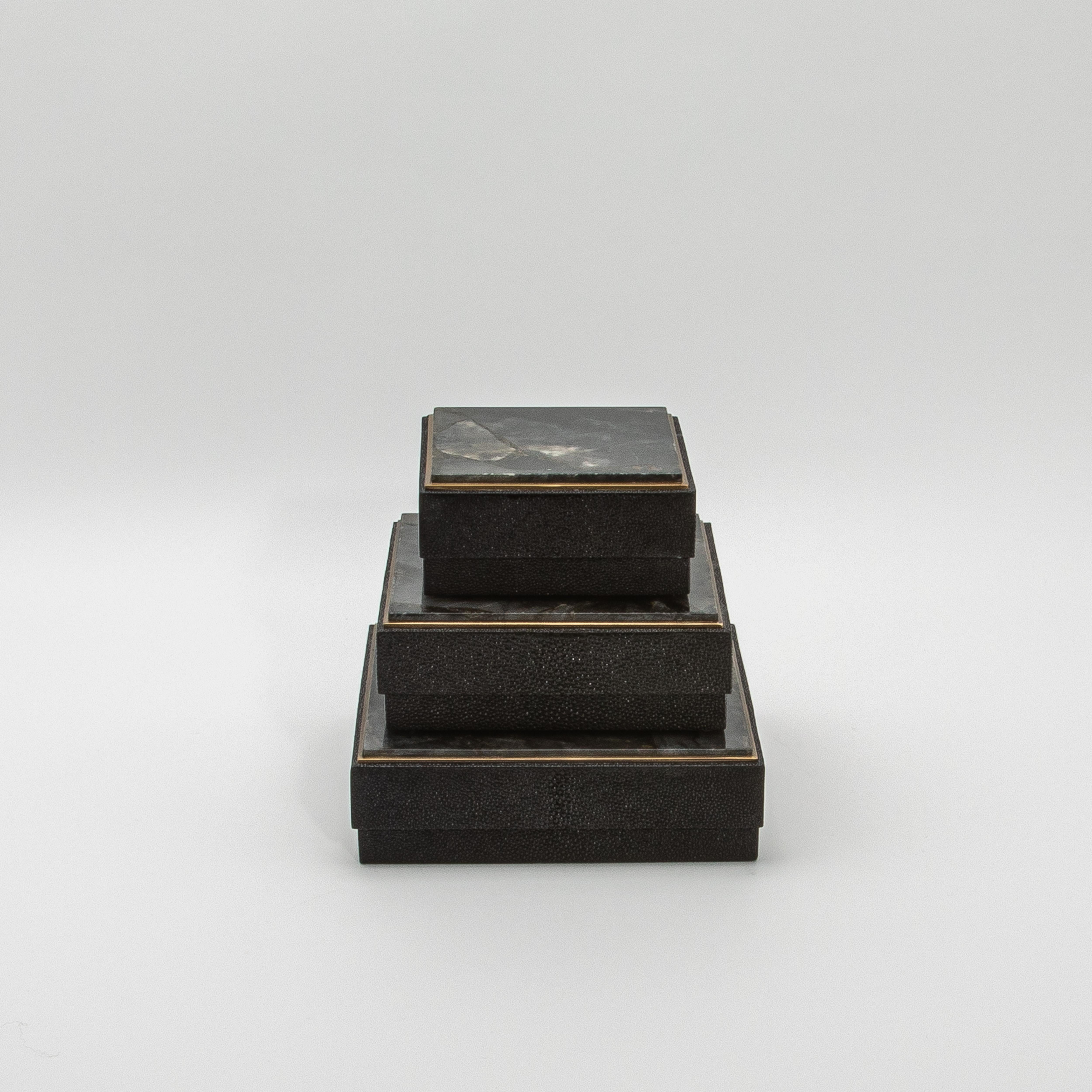 Este conjunto de tres cajas cuadradas de R&Y Augousti es un asombroso ejemplo de diseño refinado, en el que la interacción de materiales crea un cautivador contraste visual. La piel de zapa negra texturizada forma el cuerpo de cada caja, y su