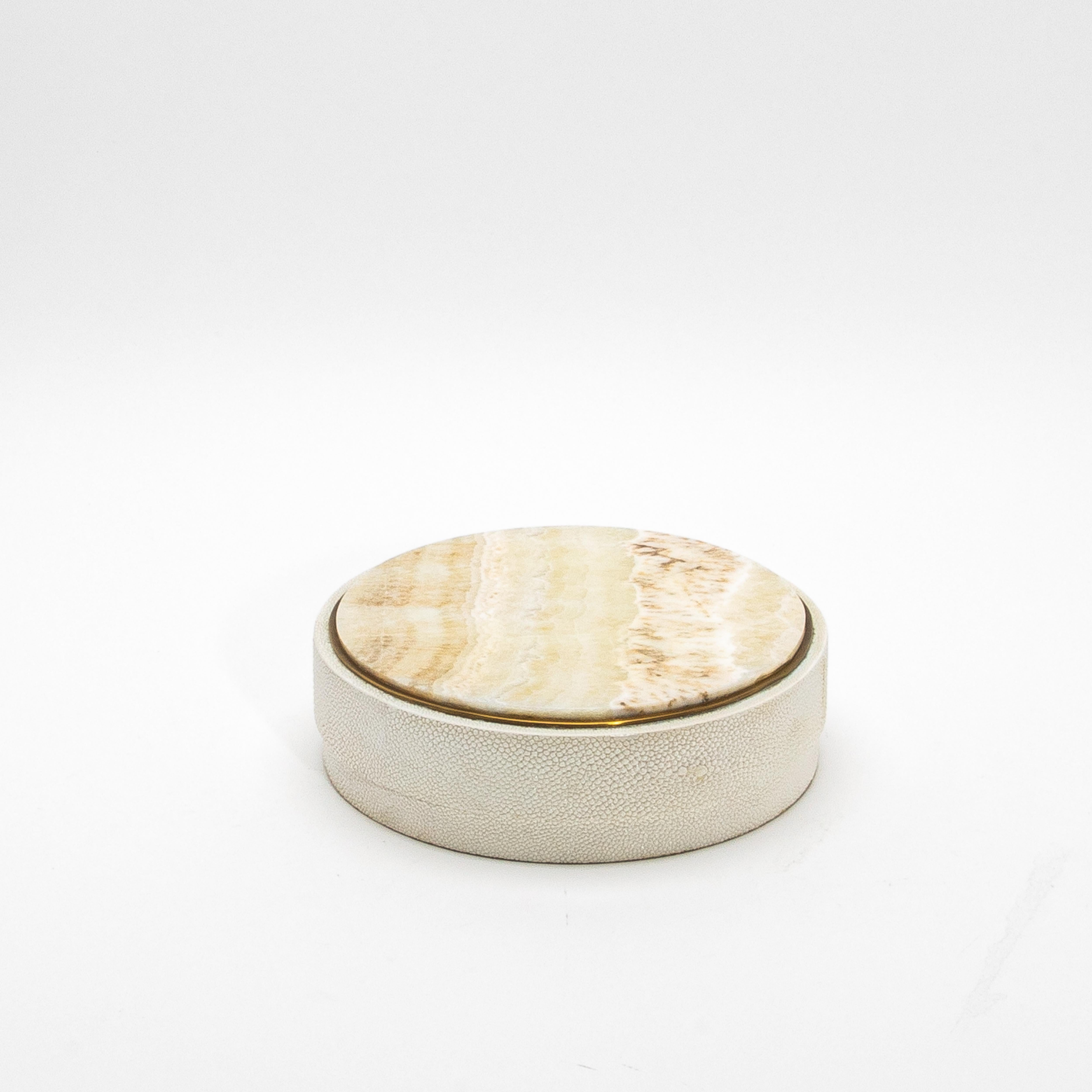 This exquisite set of 3 round boxes, crafted by R&Y Augousti, is a true testament to luxury and craftsmanship. Wrapped in a rich cream shagreen, each box features a breathtaking onyx top that radiates natural beauty, accentuated by brass details