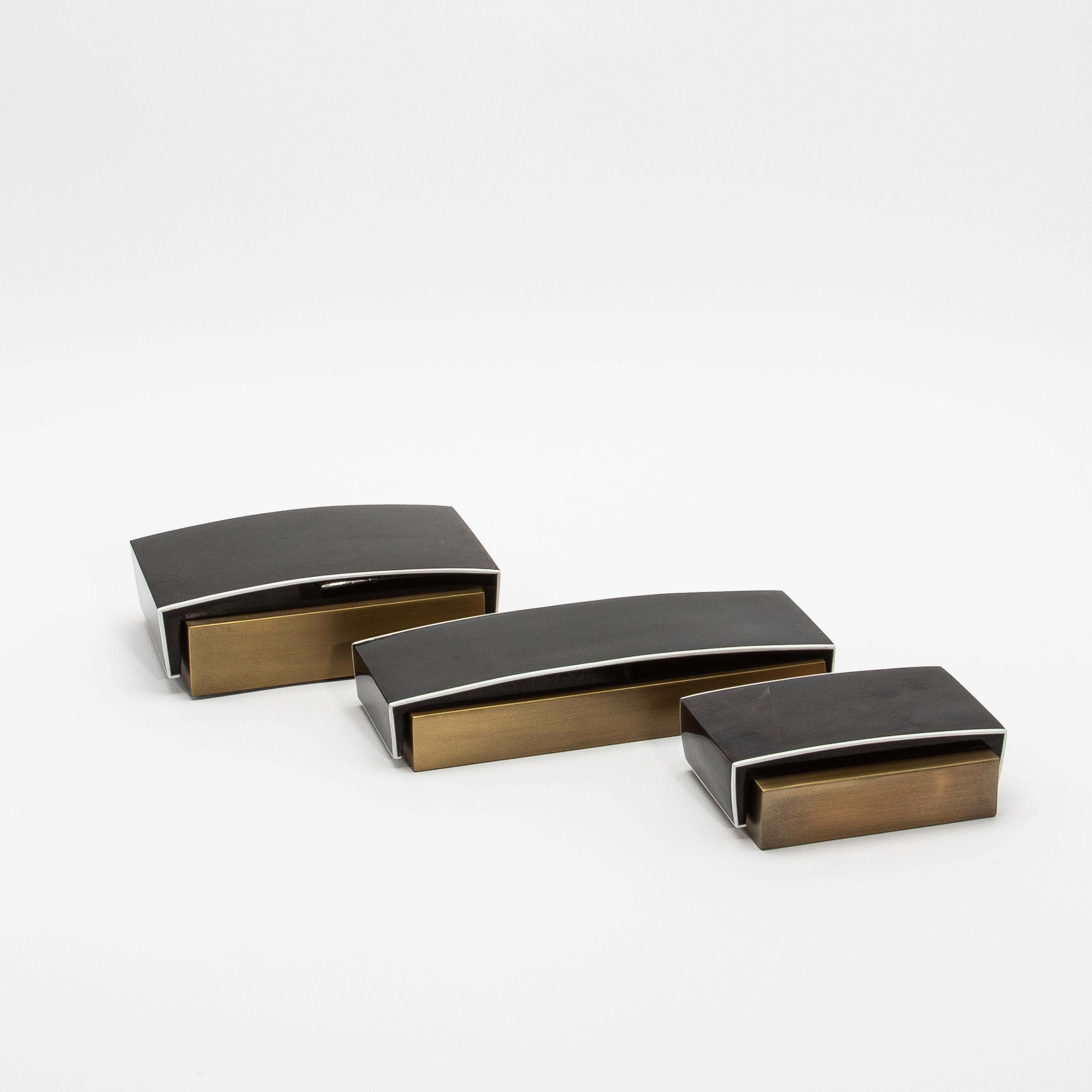 This sleek set of 3 Desk Boxes by R&Y Augousti exemplifies the perfect balance between modern elegance and timeless luxury. Crafted in black pen shell with a curved top, each box is elevated by its brass patina base, offering a bold yet