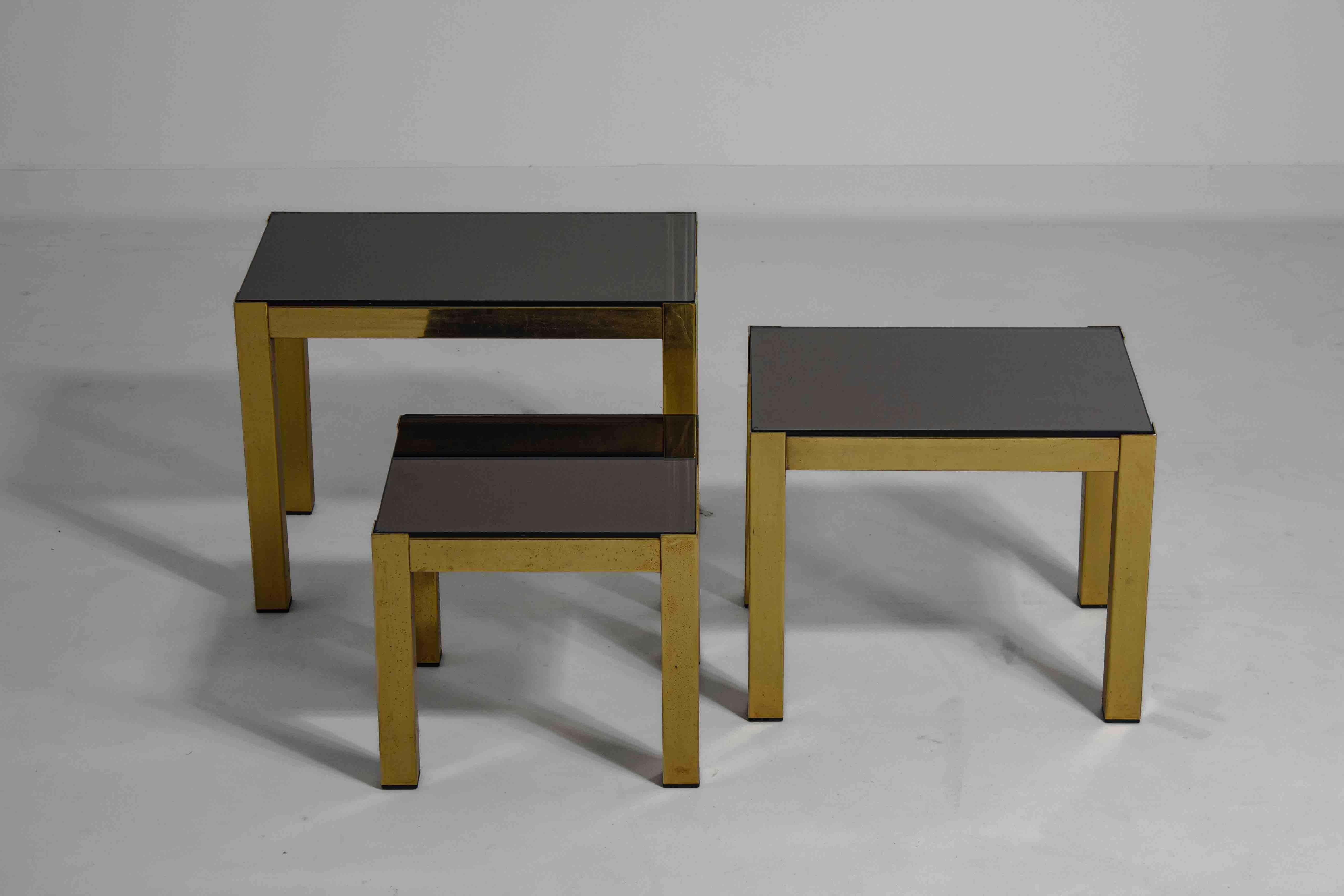 This set of brass side tables showcases the Hollywood Regency style with its clean lines and reflective surfaces. Each table features a simple, rectangular form and a mirrored top, set on a brass frame that has developed a slight patina over time.