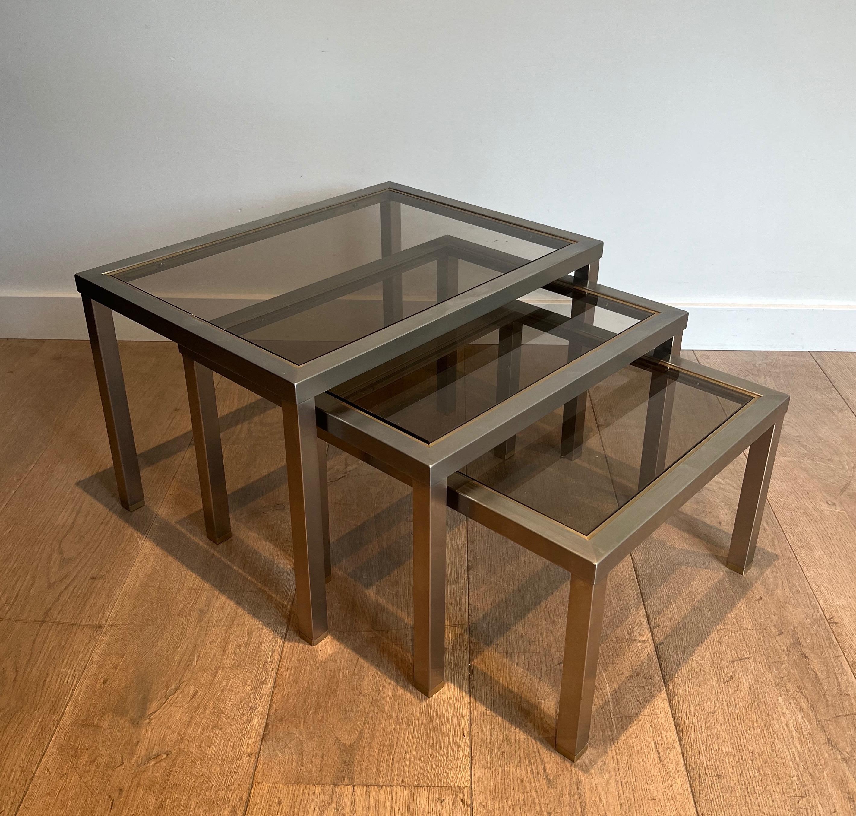 This set of 3 nesting tables is made of brushed steel and brass with bronzed glass shelve. This is a French work attributed to famous designer Guy Lefèvre. Circa 1970