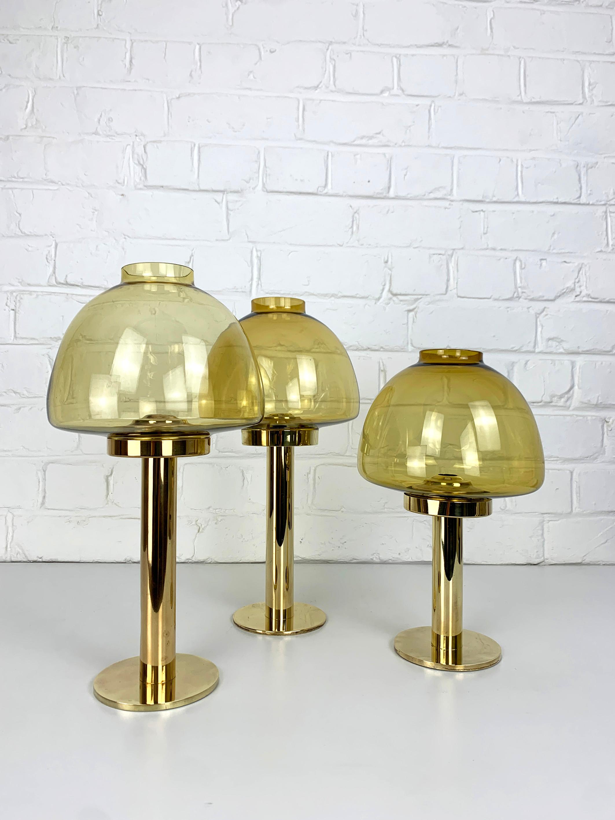 Set of 3 elegant Scandinavian L102/32 Candle Lights in brass and glass.

Nice examples of Hans-Agne Jakobsson's Candle Lanterns with their dark yellow/ochre mouth-blown glass shades. The brass base hides a spring  mechanism that pushes the candle
