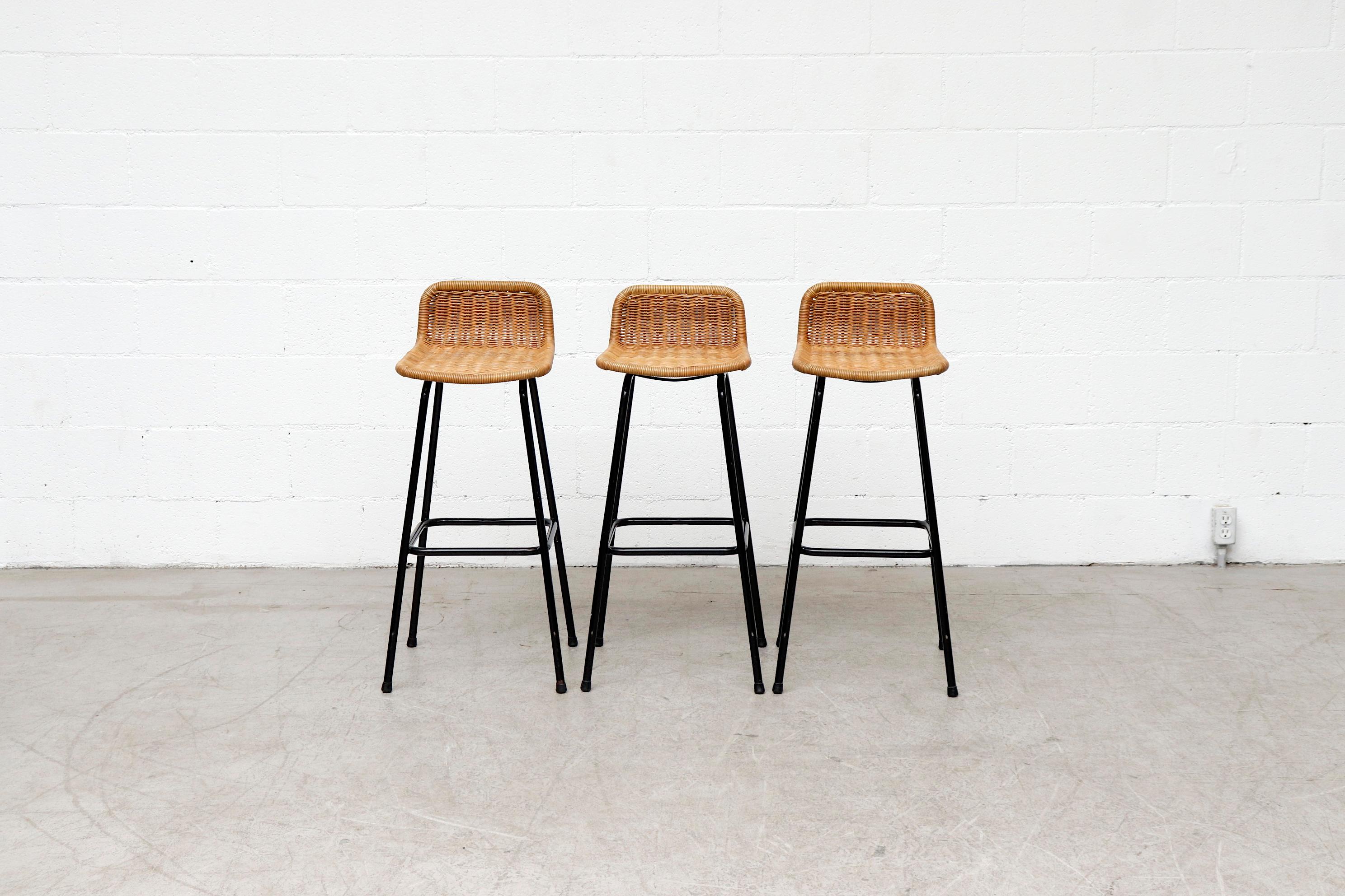 Set of 3 Charlotte Perriand style midcentury bar stools with low rounded rattan seat and back with black enameled tubular frame in original condition. 30