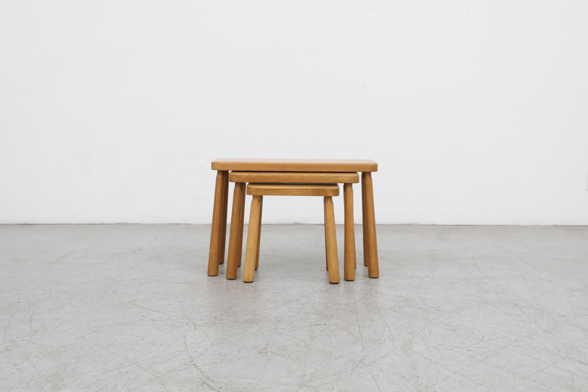 Set of 3 Charlotte Perriand style oak nesting tables with tall, round, skinny, slightly tapered legs that are wide on the bottom and narrowing at the top. The tops are solid oak with rounded edges. In original condition with wear consistent with age