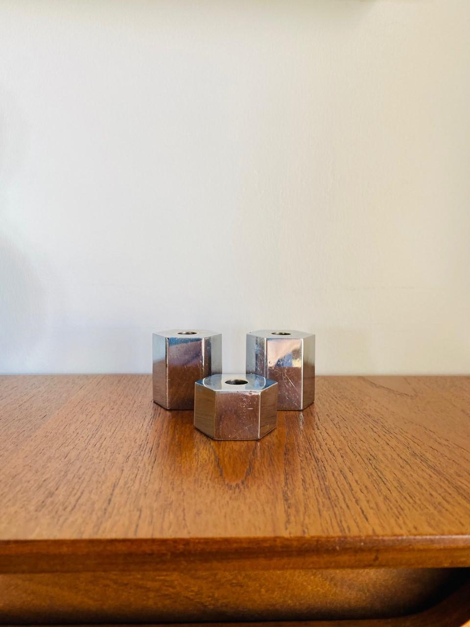 Stylish set of 3 chromed metal hexagonal candle holders. The set can be set aside with each piece of placed apart. The hexagonal design and chrome finish give a very industrial clean aesthetic. These pieces are from the 1980s and exhibit some