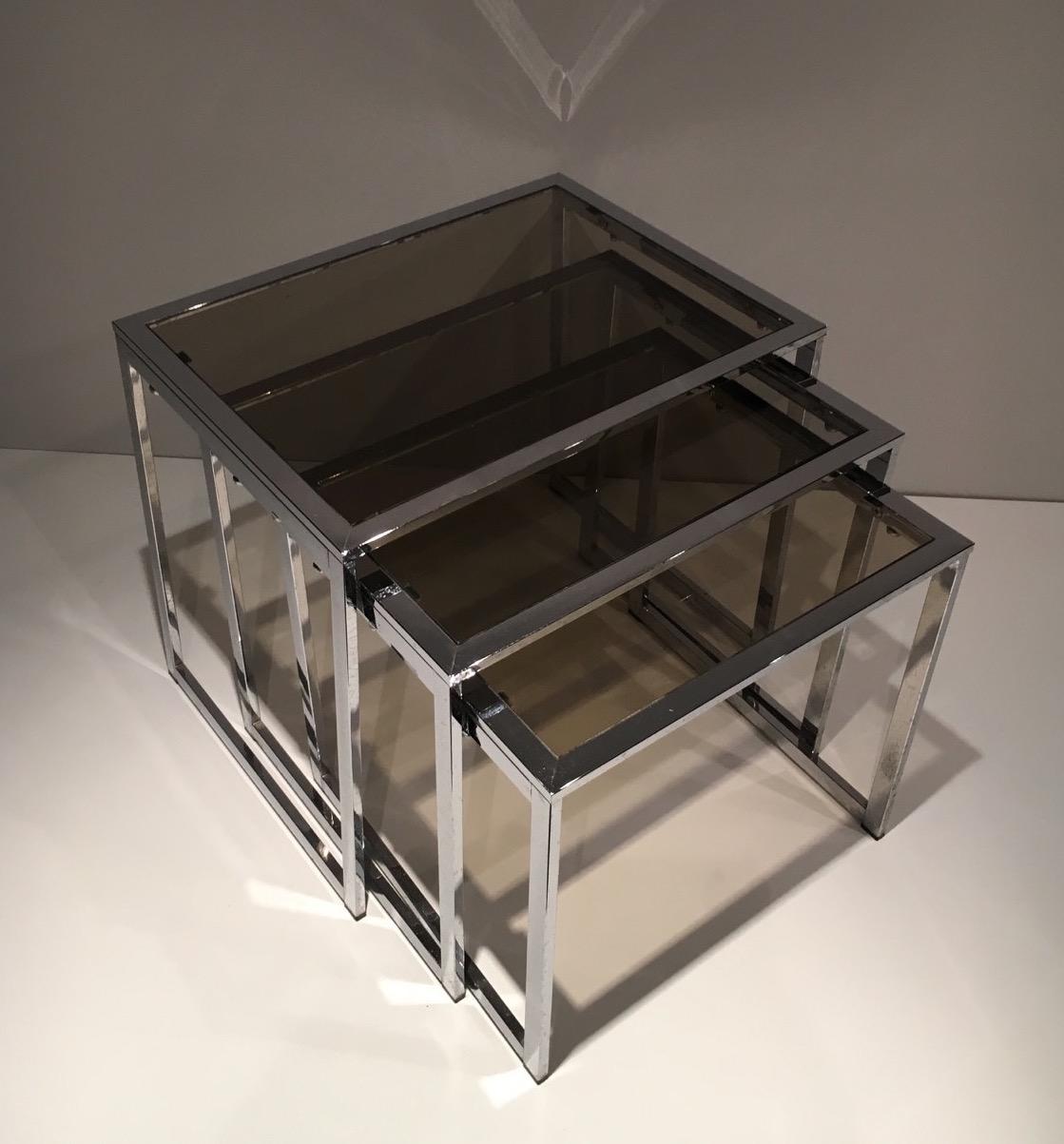 This set of 3 nesting tables is made of chrome with smoked glass shelves. This is a French work. Circa 1970.