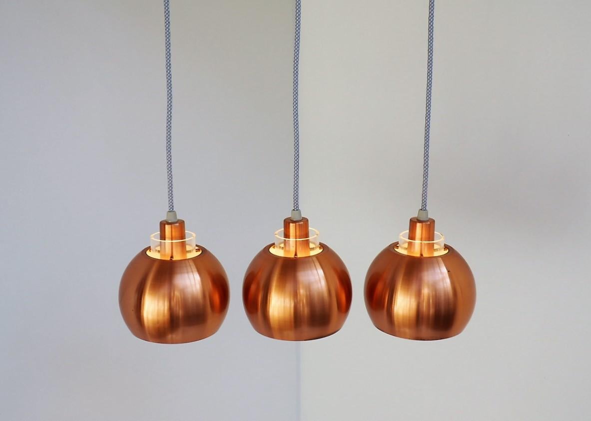 Set of 3 classic copper pendants made in the 1960s most likely by a Danish manufacturer.

The pendants are made in solid copper with white paint inside. At the top there is a transparent acrylic tube in which 3 small brass rods are mounted for