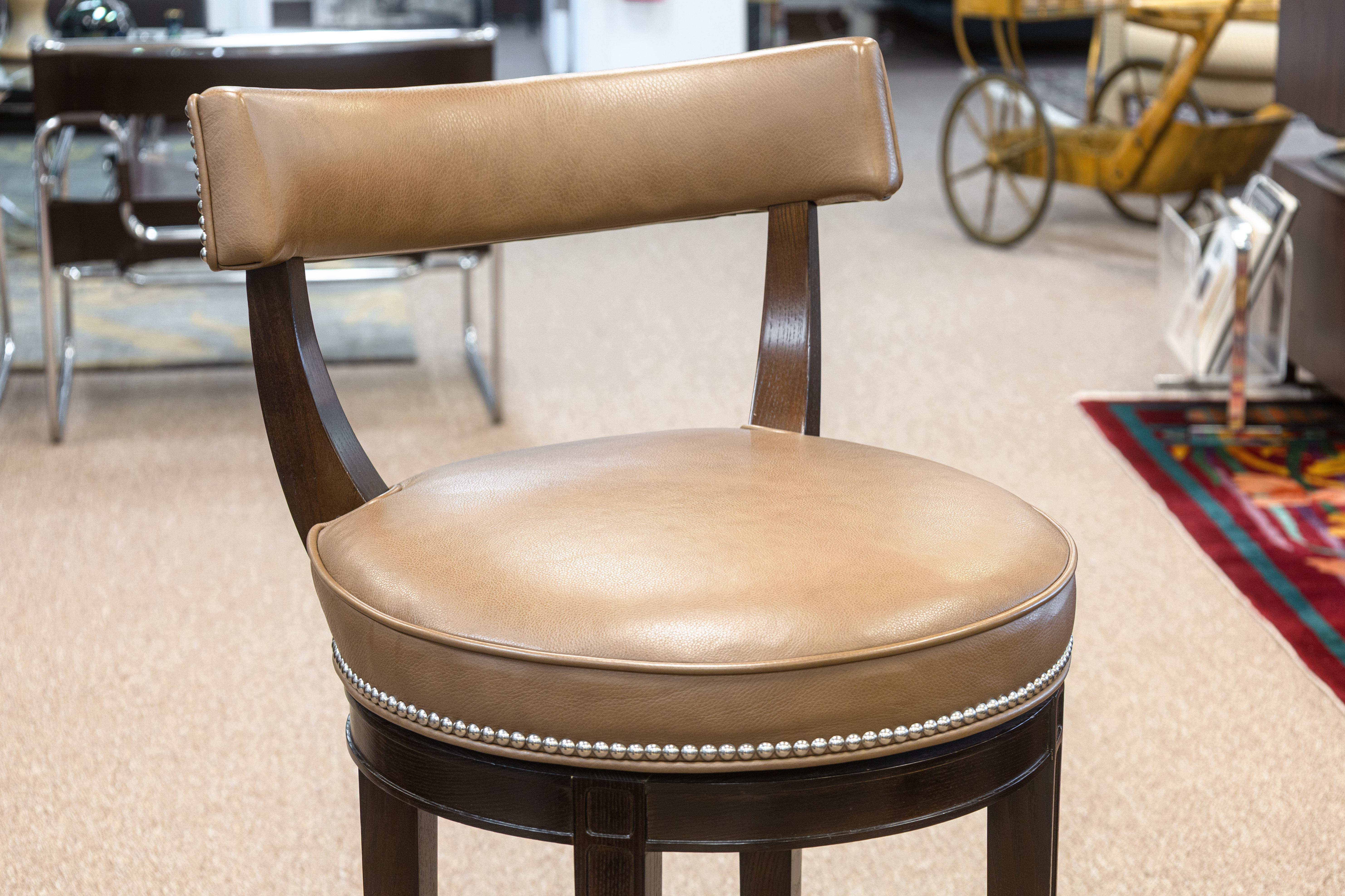 A set of 3 custom made Richard Ross Designs barstools. This set of barstools are fully custom made, with a wooden frame, brown leather cushions seats and backs with chrome rivets, and an accenting chrome footrest surrounding the four legs. The seats
