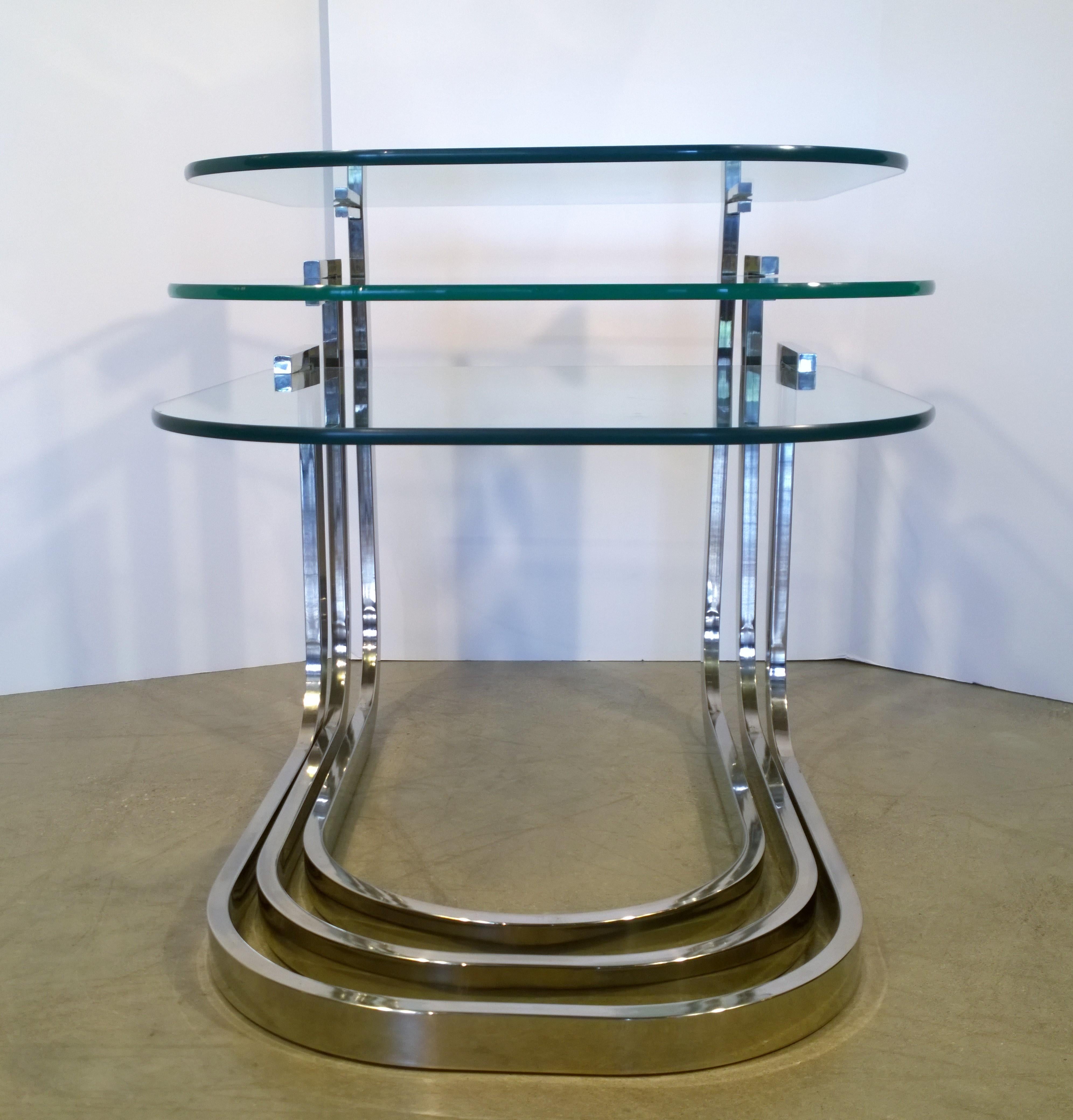 Offered is a set of three Mid-Century Modern Design Institute America glass and chrome stacking tables. This set of three chrome and glass stacking tables are a true example of DIA's Classic modernist vision. The horseshoe shape of the chrome and