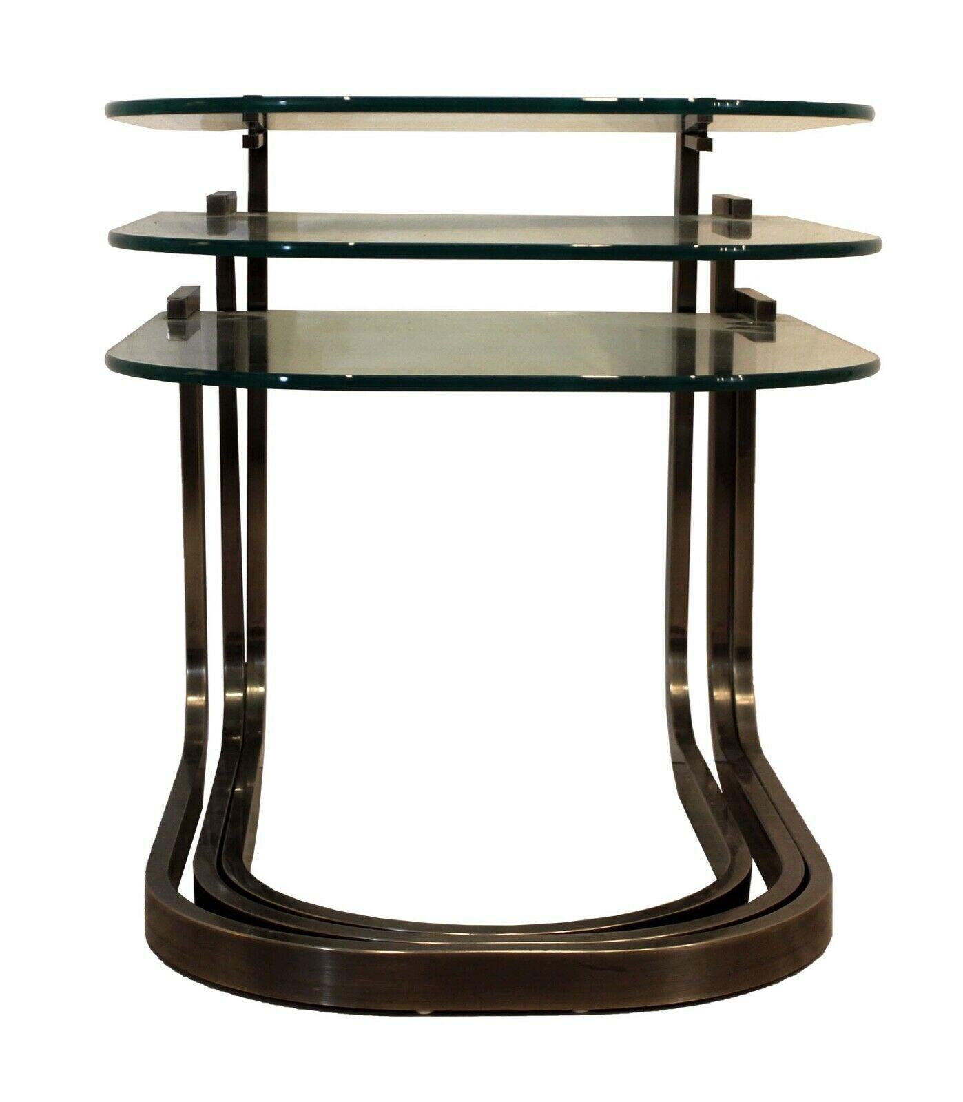 From the Design Institute of American (DIA), this set of three tables nest neatly together to create a sculpture profile of glass tops supported by bent, brushed pewter frames. In good condition, this set shows wear consistent with age as noted in