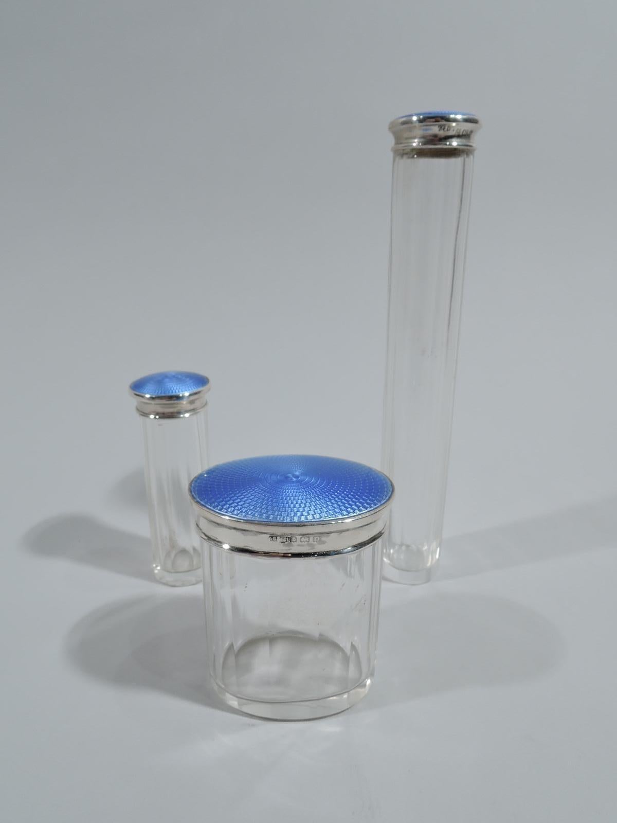 Set of 3 English Art Deco glass vanity jars with sterling silver and enamel covers. Each: Faceted and straight sides. Cover top has concentric guilloche enamel ornament. Cover sides sterling silver. Enamel is blue. Glass is clear. One jar is oval