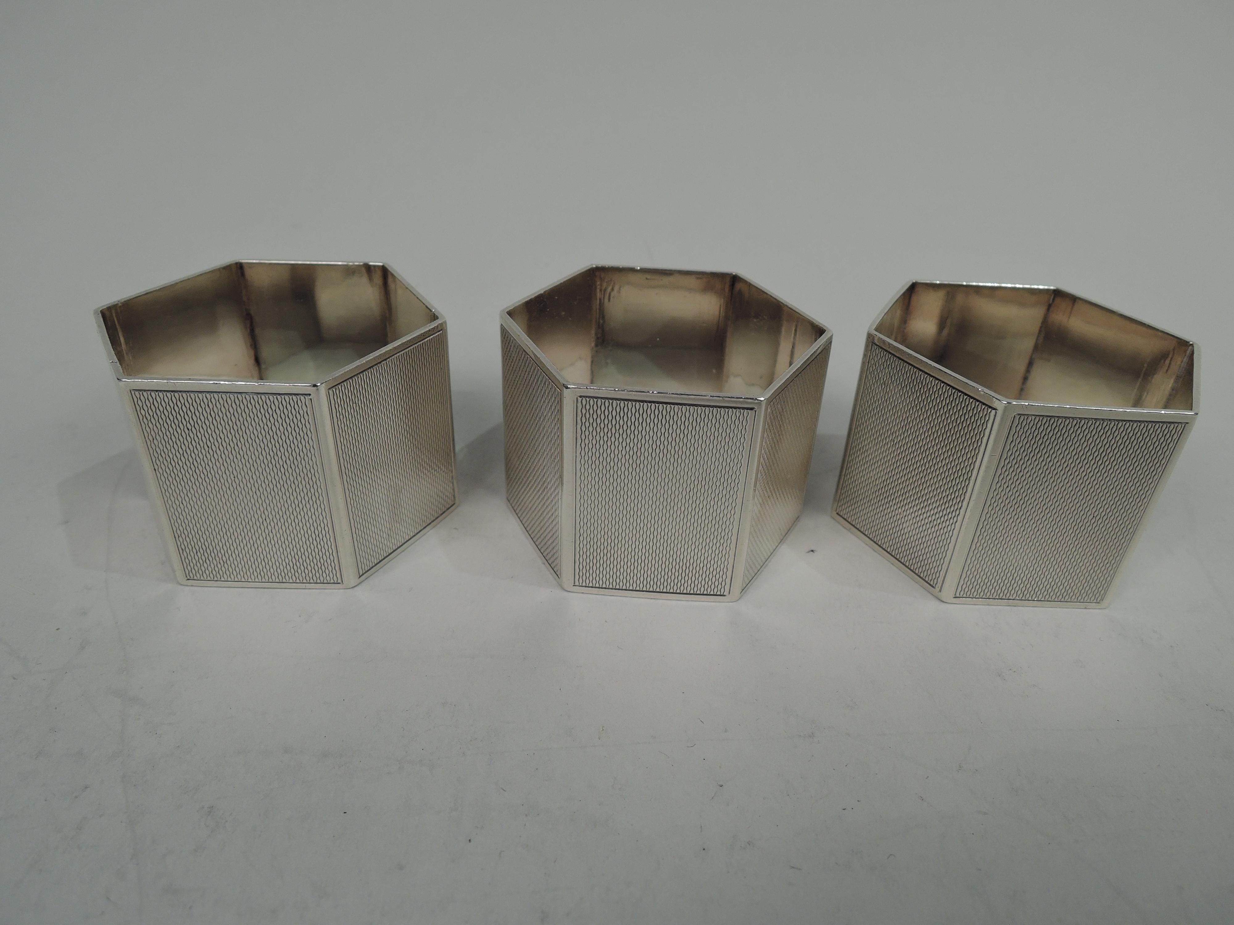 Set of 3 George VI sterling silver napkin rings. Made by Turner & Simpson Ltd in Birmingham in 1939. Hexagonal with allover engine-turned ornament in thin plain frames. Letter block monogram on lined ground. Each has a different letter: F, G, and L.