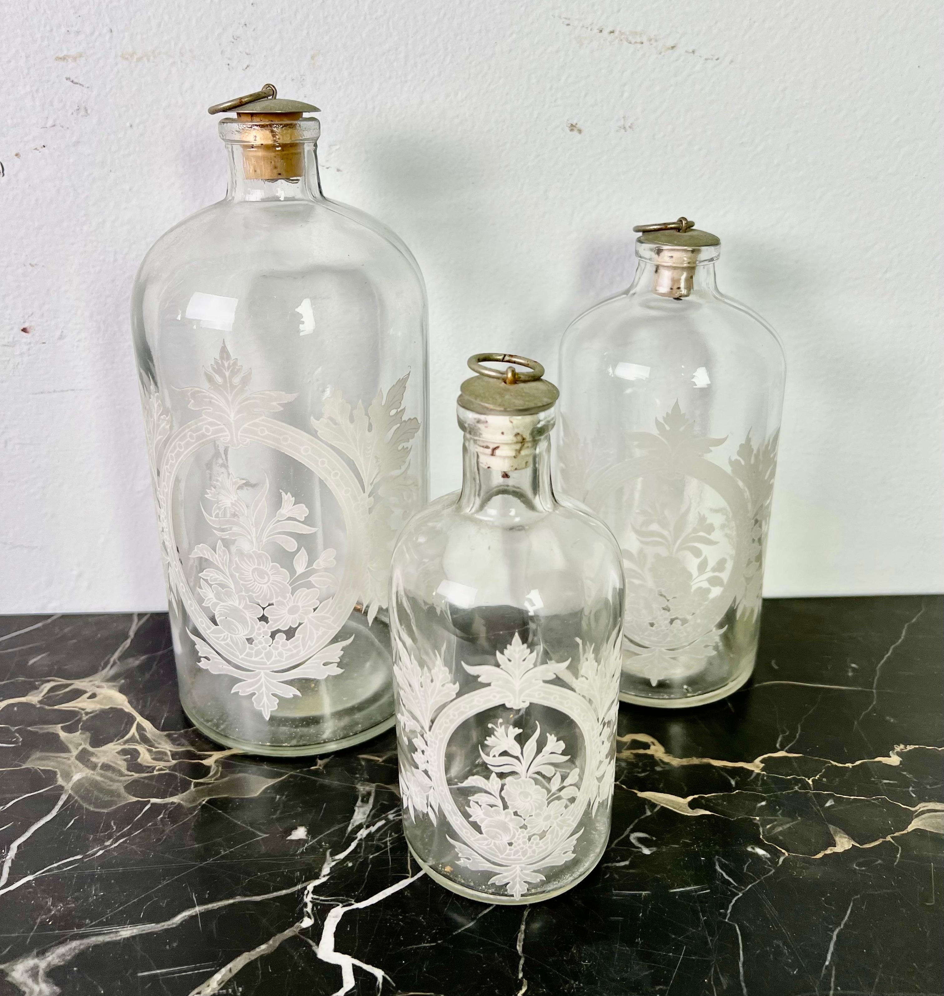 Set of (3) vanity bottles with cork tops. The bottles are etched with beautiful white flowers throughout. There are three different sizes:

Large-8.5