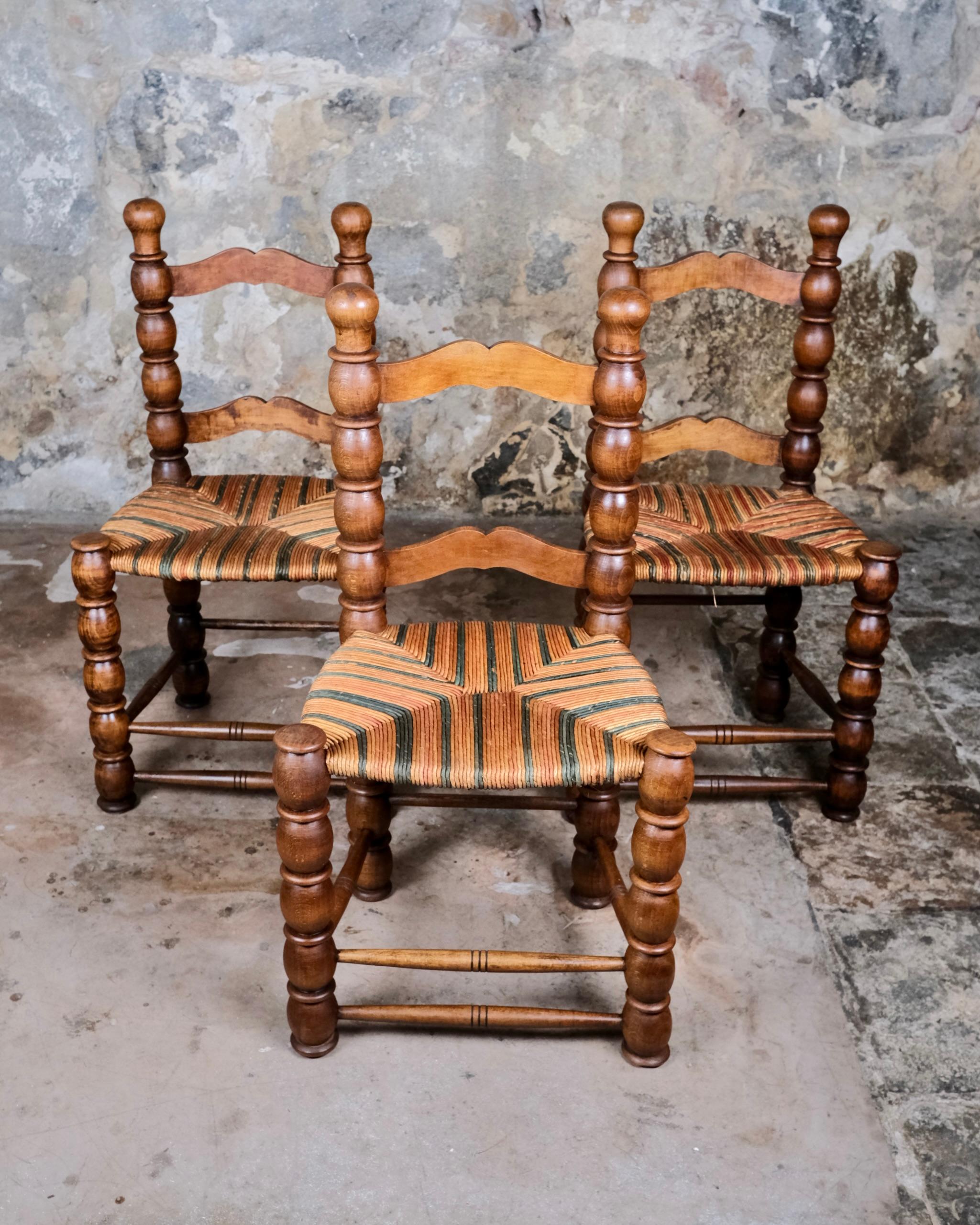 An exceptional and rare set of 3 French bobbin turned chairs dating from the 1940s–1950s, crafted in solid oak with vibrant multicolored straw seats. Inspired by the distinctive design language of Charles Dudouyt, these chairs are a celebration of