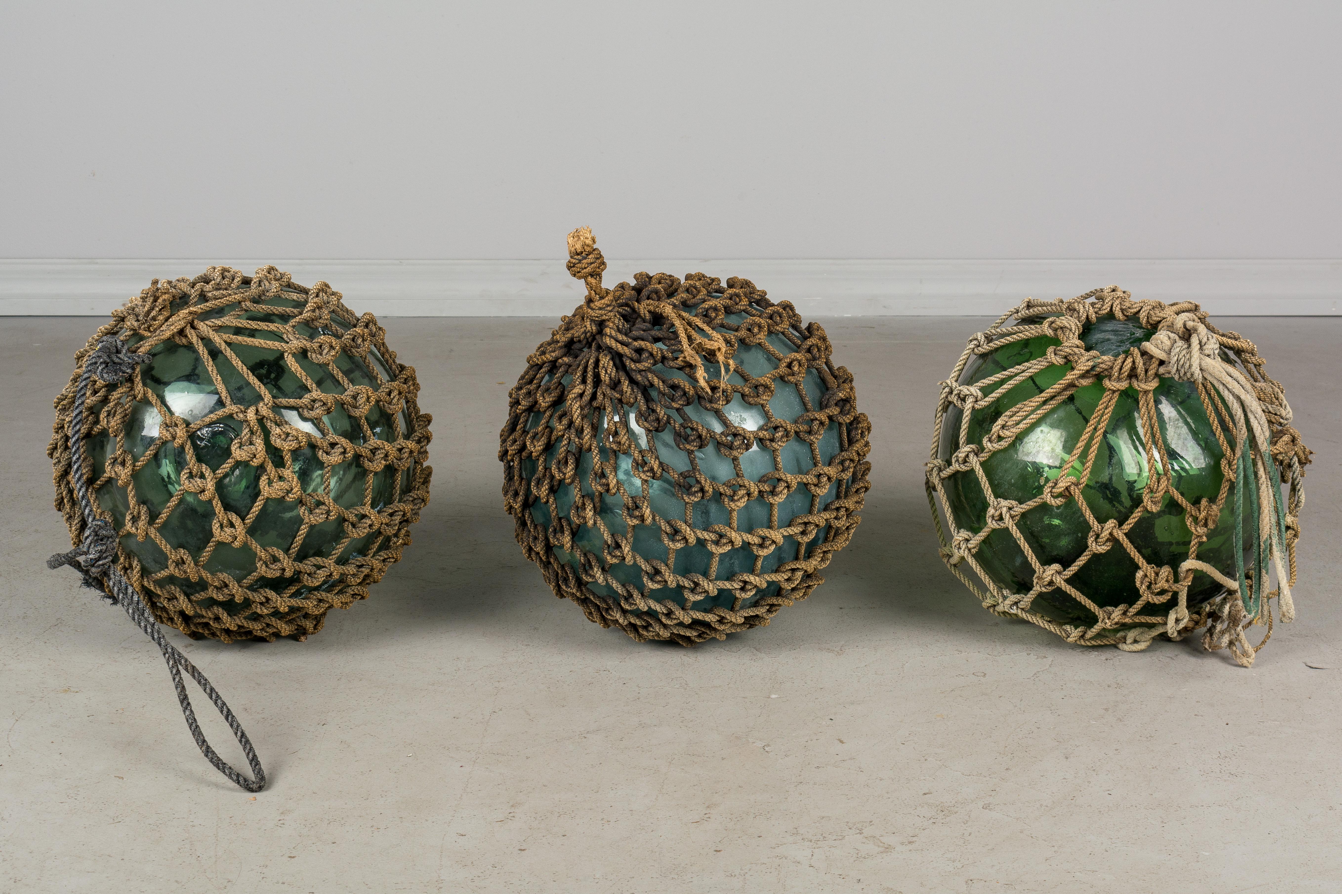 A set of three glasses Japanese fishing floats. These large hand blown globes were made from recycled glass bottles encased in tightly knotted rope and were used to buoy a fisherman's net when cast into the water. The rope varies in condition with
