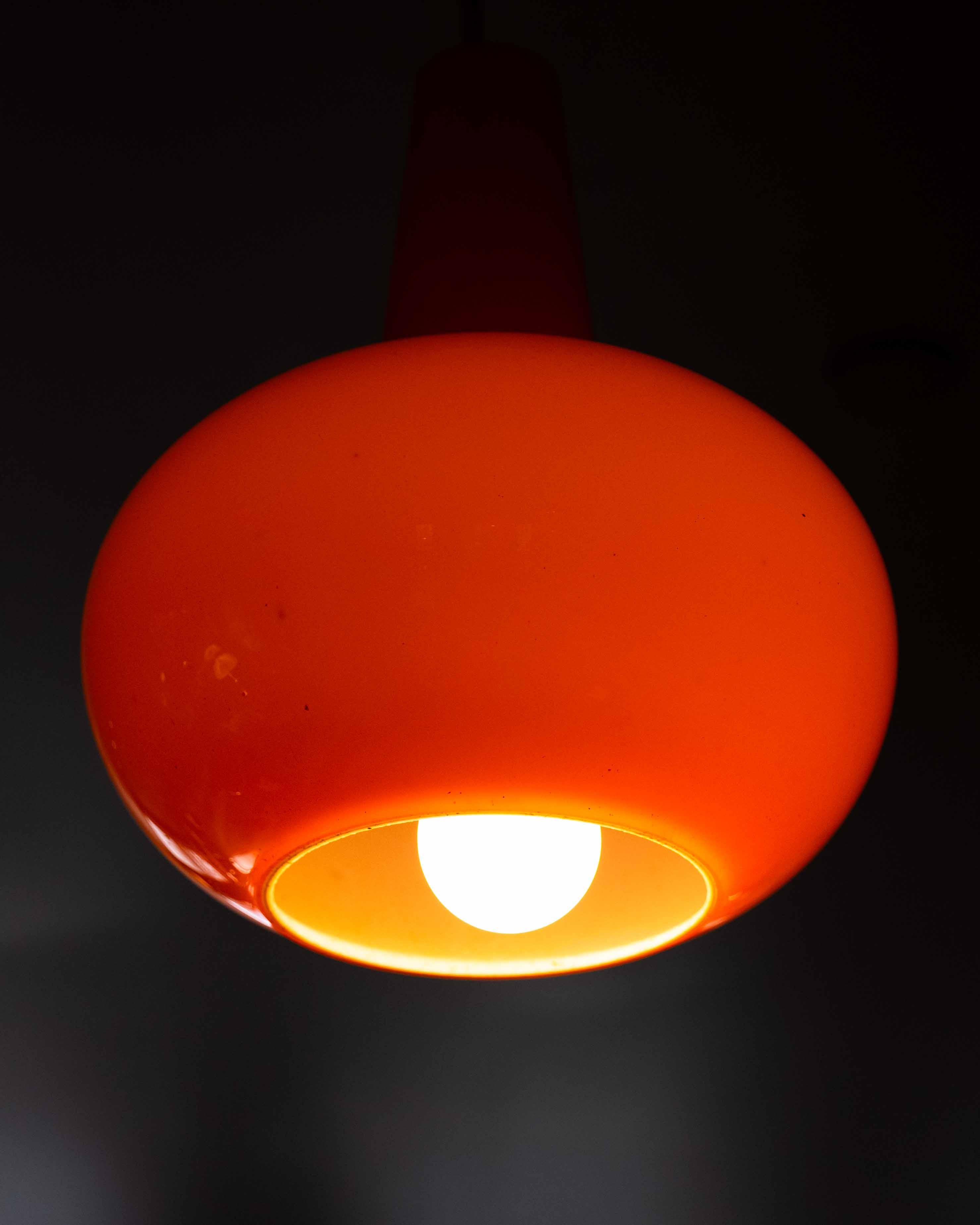 Set of three Mid-Century Modern pendant lights, crafted from vibrant colored glass in bold primary tones—red, orange, and black. Each pendant features a rounded bottle-like silhouette with a high-gloss finish, adding a playful yet refined pop of