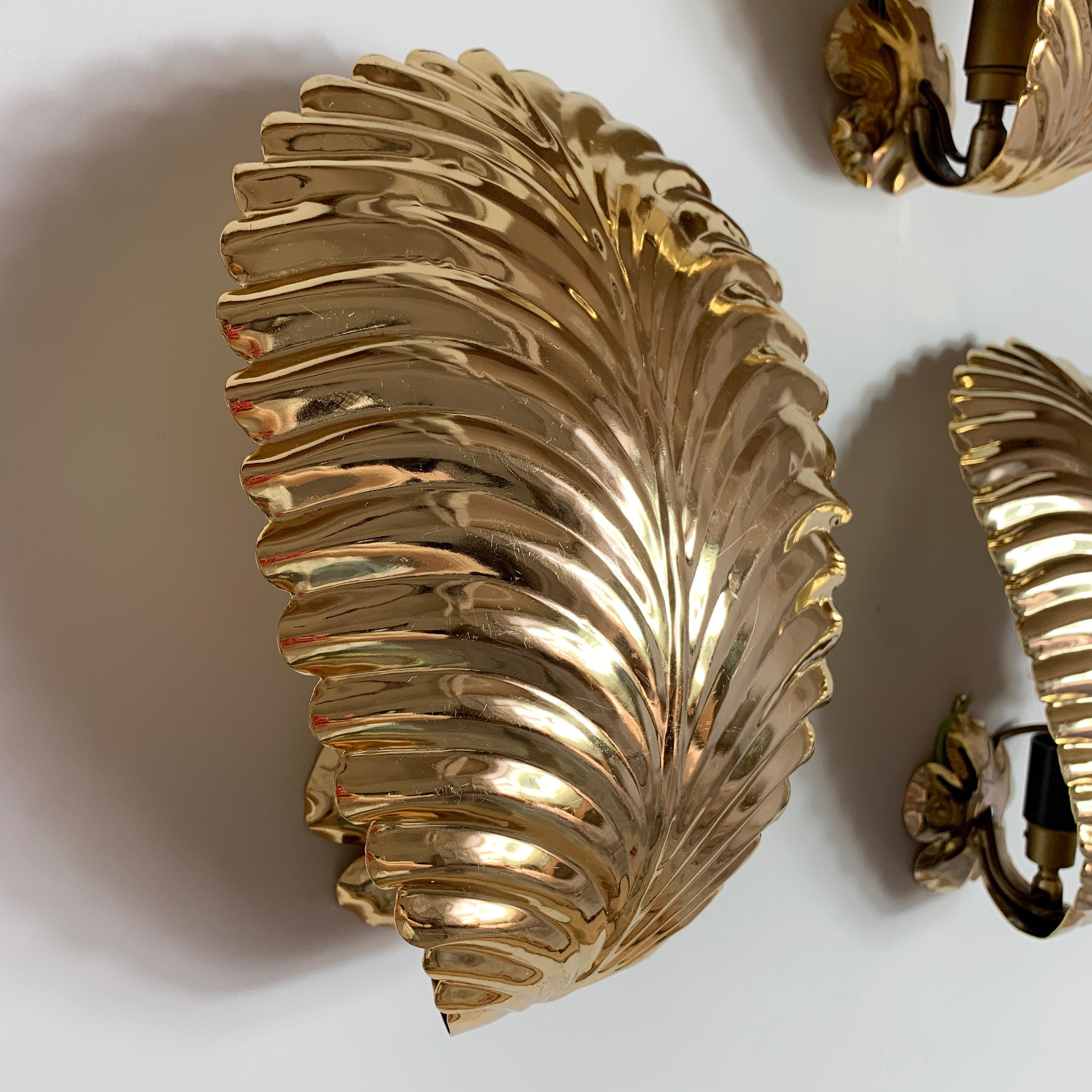 Set of 3 gold palm leaf wall lights.
1980s.
3 large individual shiny gold metal palm leaves.
Behind each leaf a single E27 bulb holder is hidden.
There is a ring hanging hook on the back of each light to attach to the wall.
Measures: 19.5cm