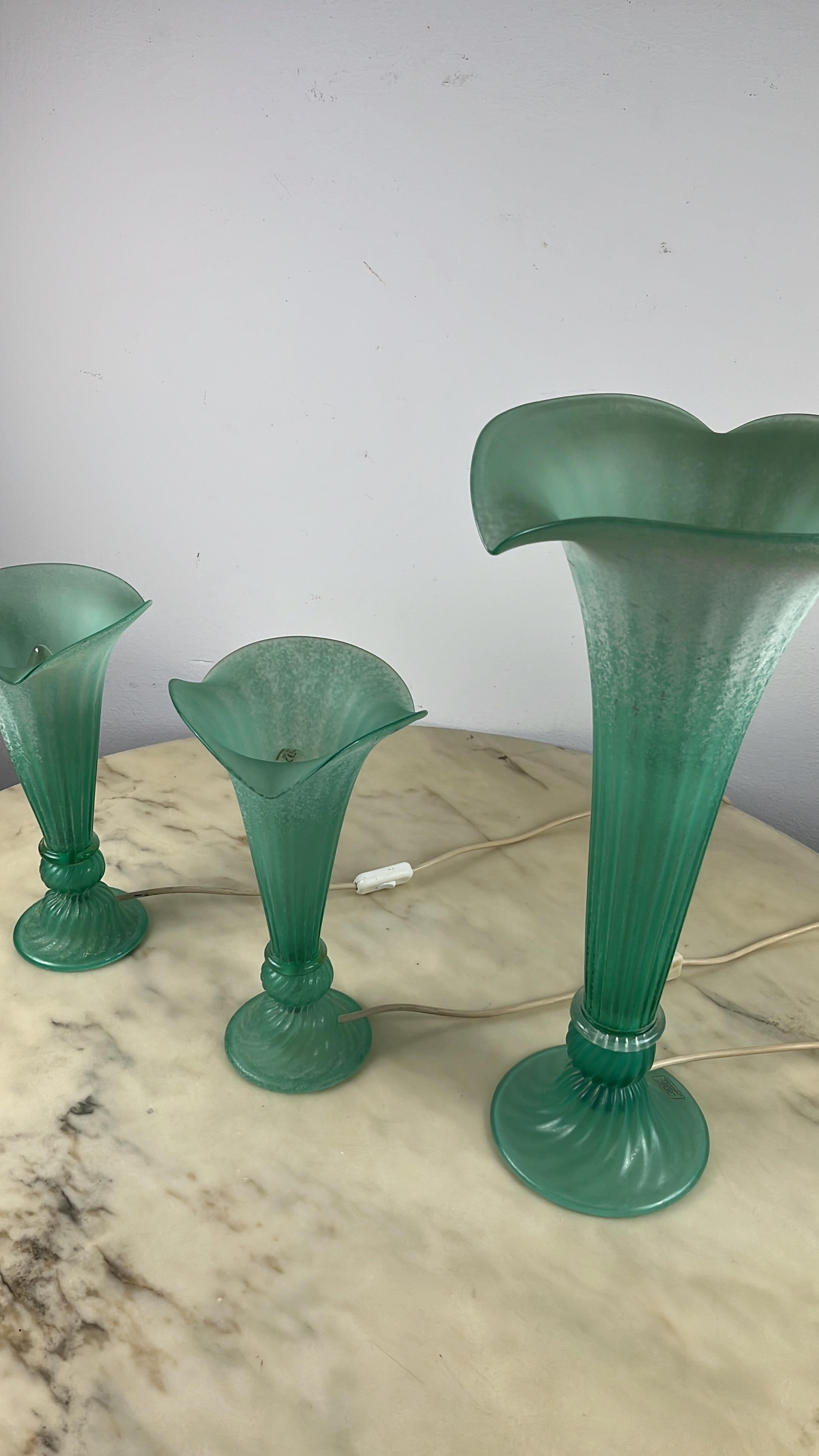 Set of 3 green Murano glass lamps, Italy, 1980s.
The large one is 53 cm high and measures 27 cm in the widest part. The two smaller ones are 33 cm high and measure 18.5 cm in the widest part.
They are shaped like flowers. Intact, working and in
