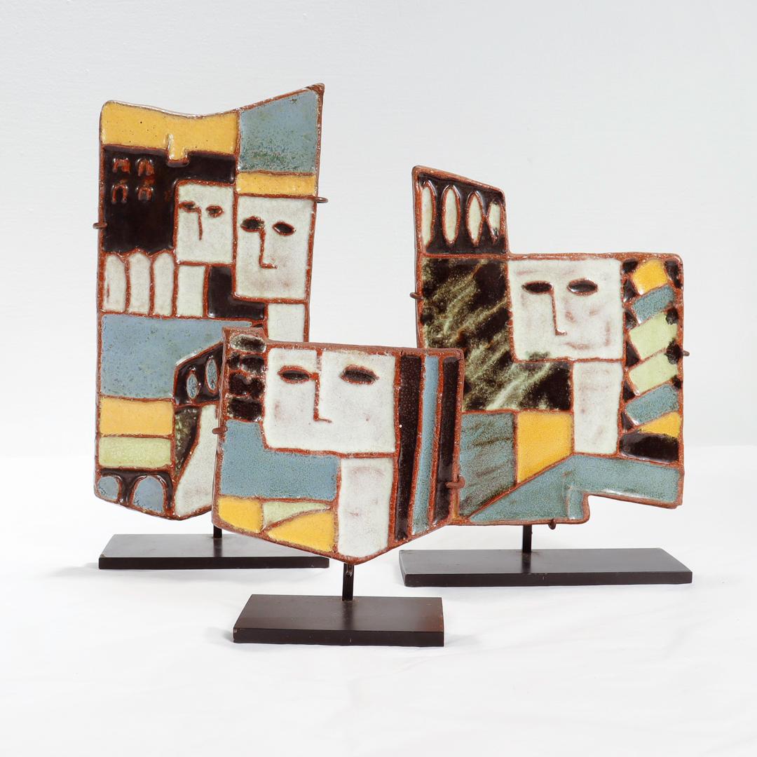A fine set of 3 Mid-Century Harris Strong pottery tiles.

In terracotta pottery with polychrome glazes in teal, custard, turquoise, white, & chocolate brown tones. 

Set on sturdy black painted metal museum displays.

Simply a wonderful set of
