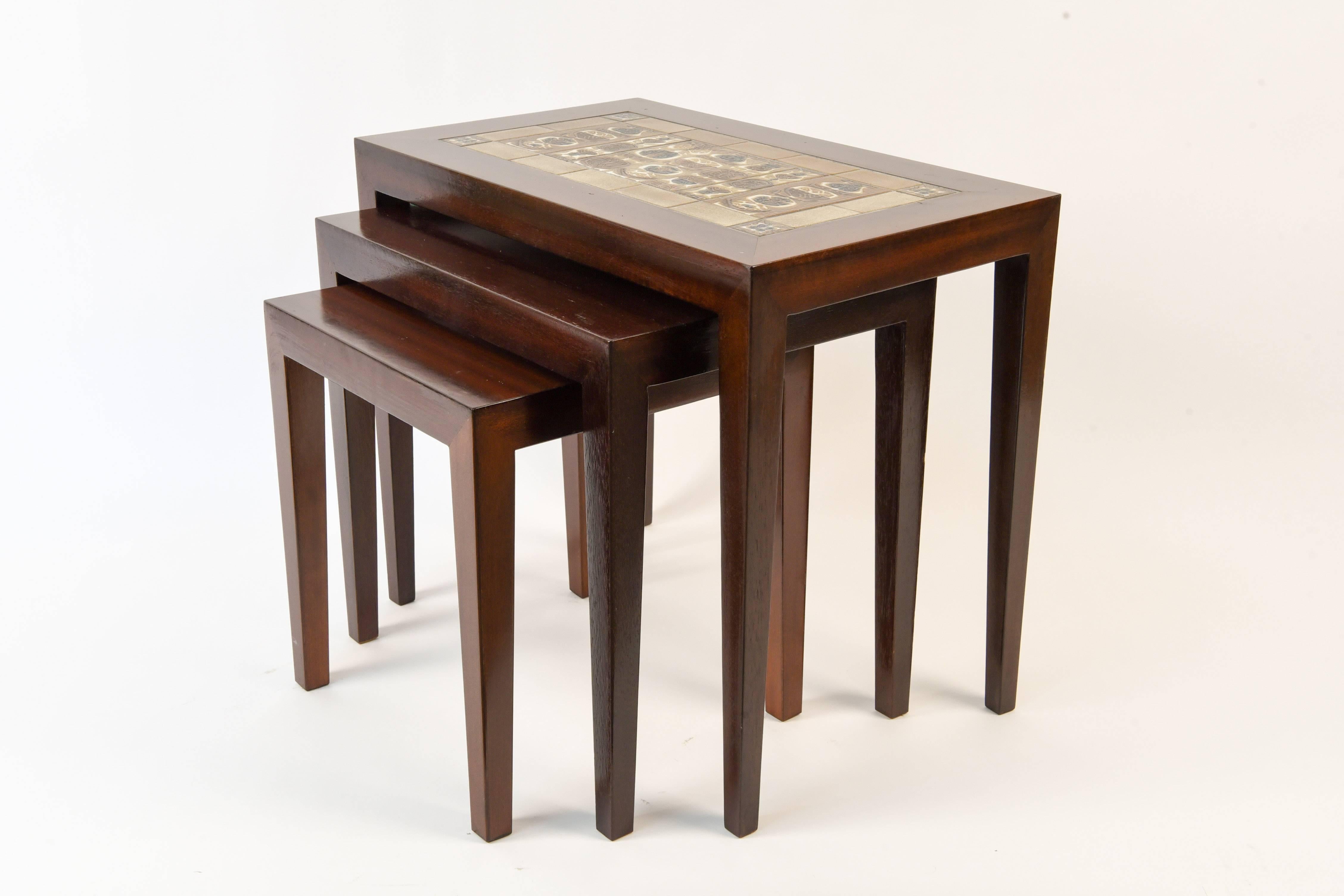 This set of three mahogany nesting tables features a tile top with tiles designed by Nils Thorsson for Royal Copenhagen as part of the Tenera series. Beautiful color to the mahogany wood, with a great artistic feature of the tiles.