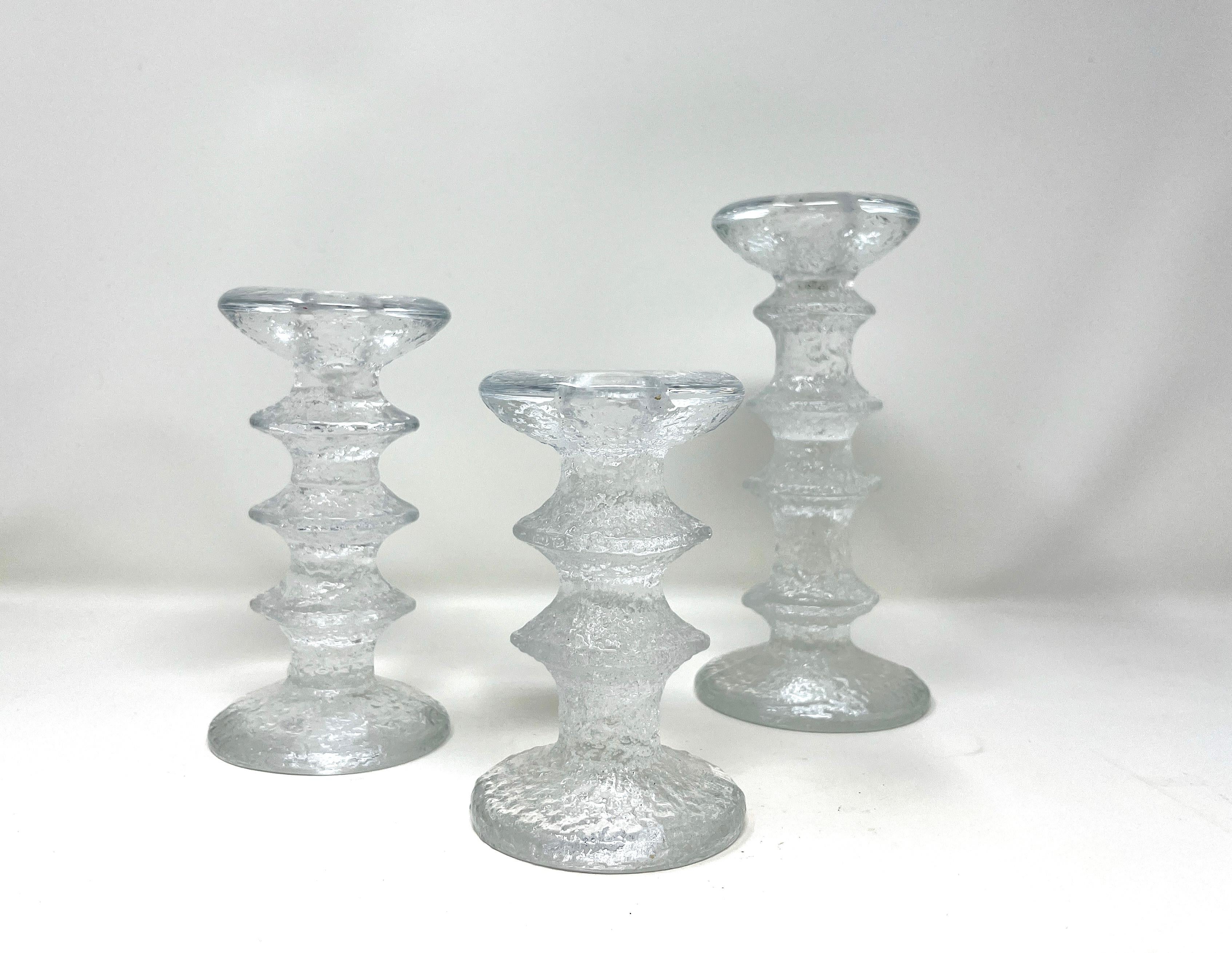 Set of 3 staggered in size Iittala candlesticks. Textured clear molded glass composed as a column with projecting bands, a flared mouth and a round base. Designed by Timo Sarpaneva for Iittala, Finland. A beautiful, classic Scandinavian Modern