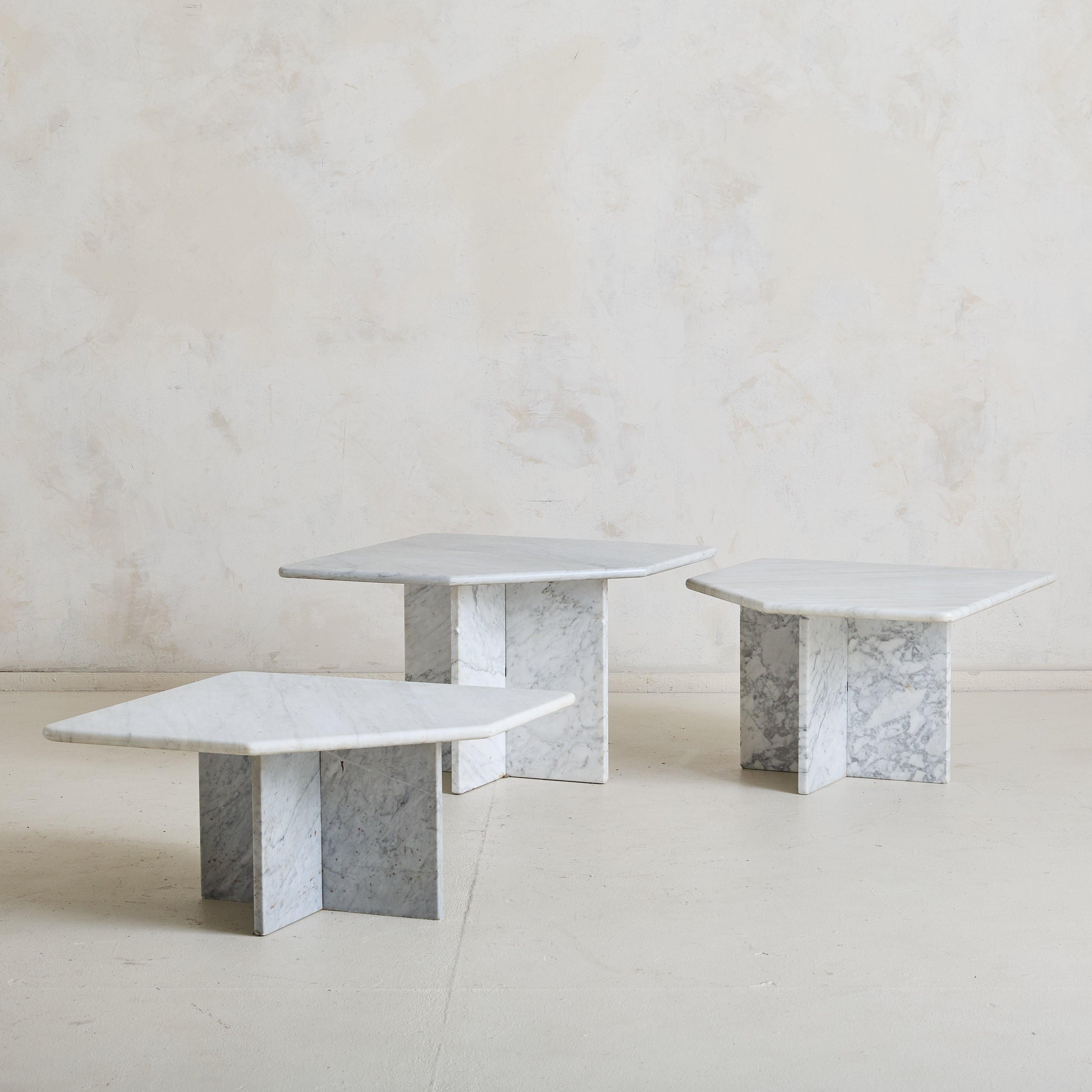 A trio of 1970s Italian nesting tables, expertly crafted from solid Carrara marble. Each tabletop, oblong in form, showcases the natural beauty of the stone with its soft white surface and delicate gray veining. Resting on four-point pedestal bases,