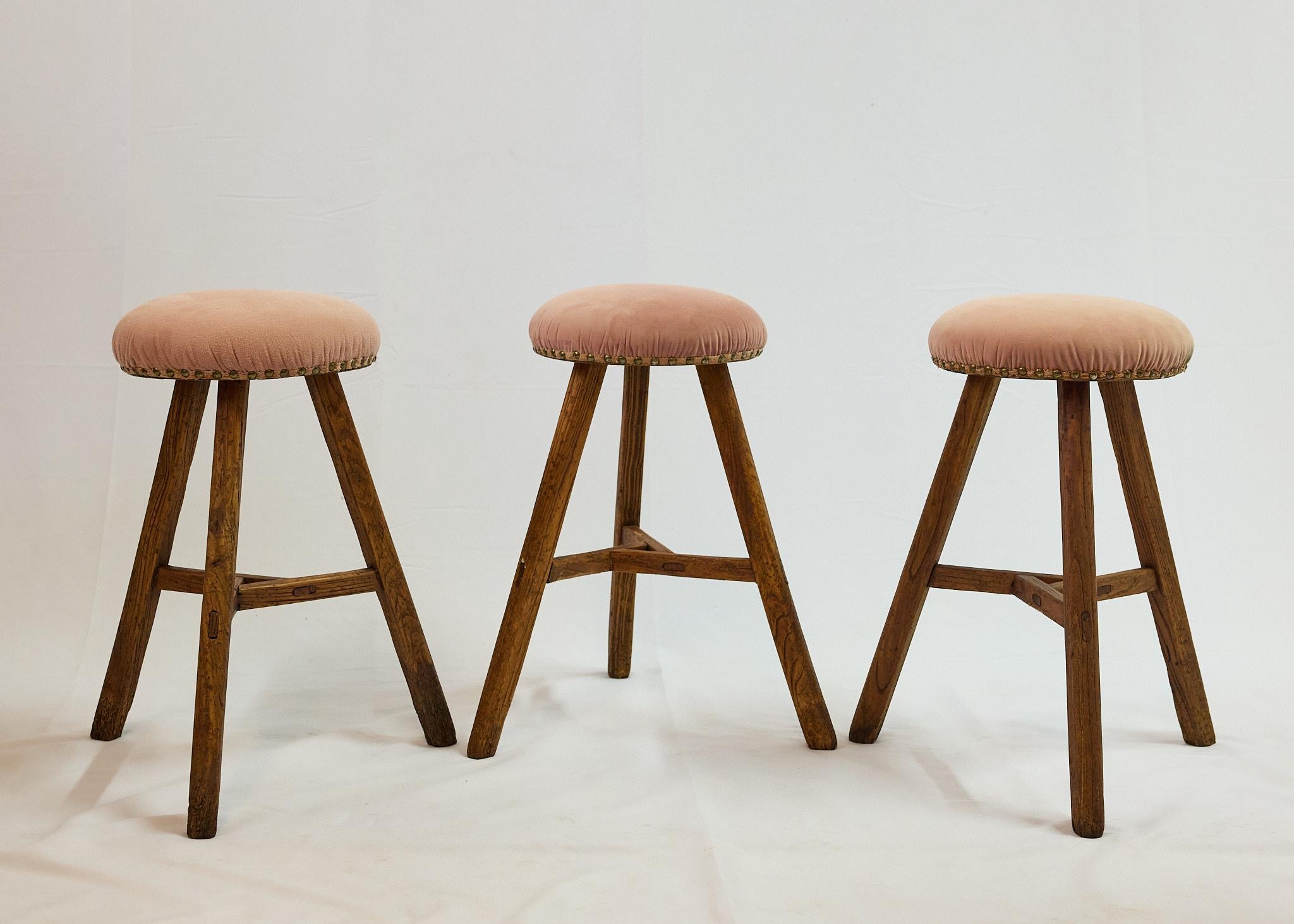 Set of three early 20th Century Italian milking stools with great primitive form and modern lines. Each stool has three wooden splay legs that are pegged together by a triangular apron at its center. The round wooden seats are padded and upholstered