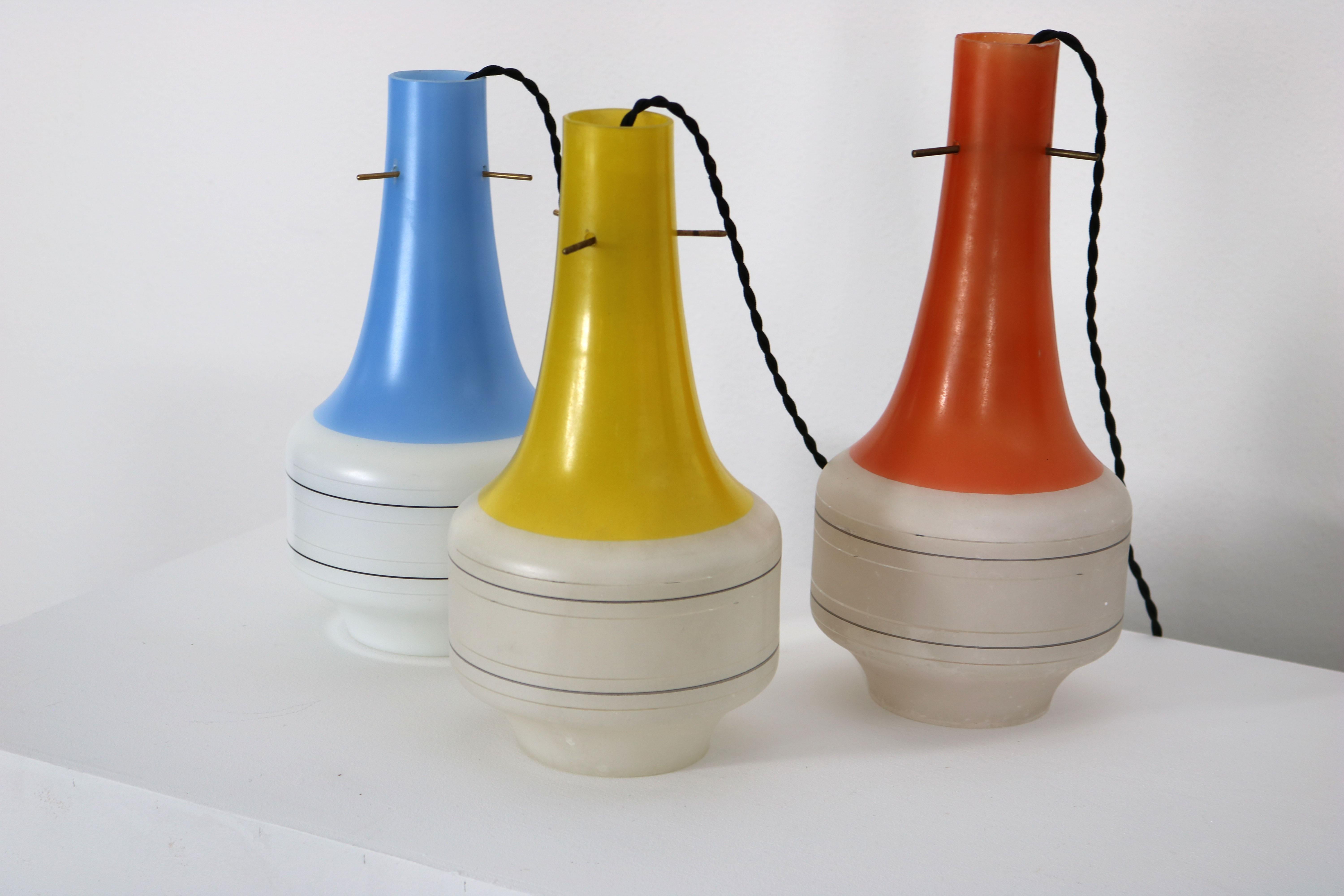 This Italian set of three glass pendant lamps dates back to the 60s. The Vistosi style set has three different colours, red yellow and blue. While the upper parts of the lamps are coloured, the lower parts are in matt white glass. The fabric cables