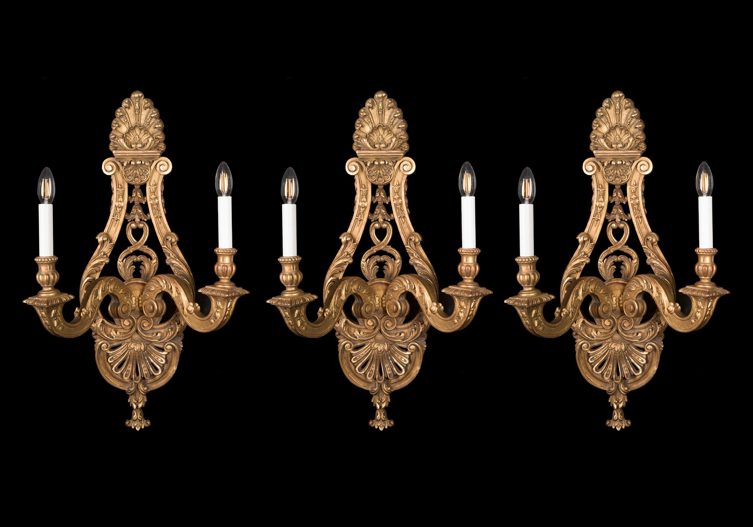 A very fine set of three large giltwood wall sconces in the Régence style, ornately carved with foliate flourishes and palmettes, and swan neck twin branches.

French, early 20th century.