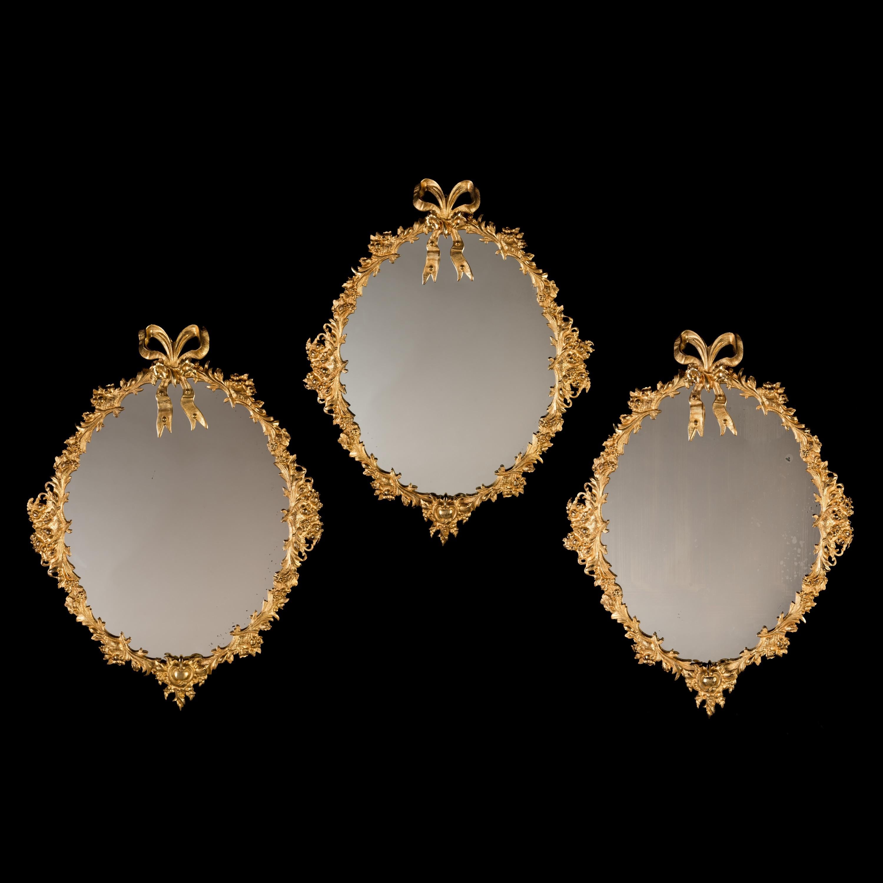 Un set di tre specchi inglesi in ormolu

I piatti ovali in vetro specchiato sono alloggiati in cornici di bronzo dorato ben fuse, con fogliame d'acanto sovrapposto e intervallato da fiori e bacche; ogni specchio è sormontato da un nodo d'amore o da