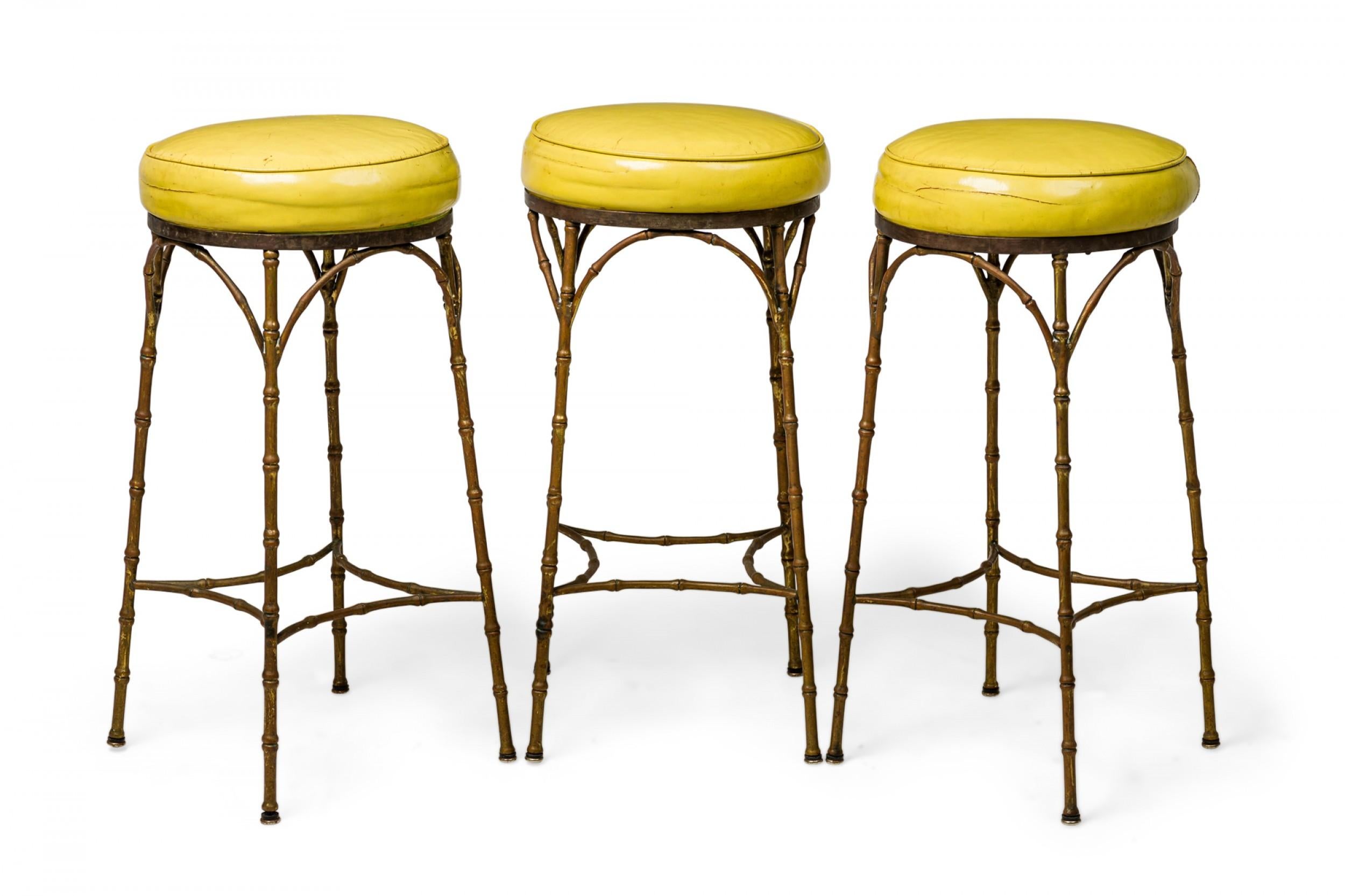 Set of 3 Mid-Century American brass faux bamboo yellow leather upholstered bar stools with incurved supports. 

Wear to finish. Worn seats.