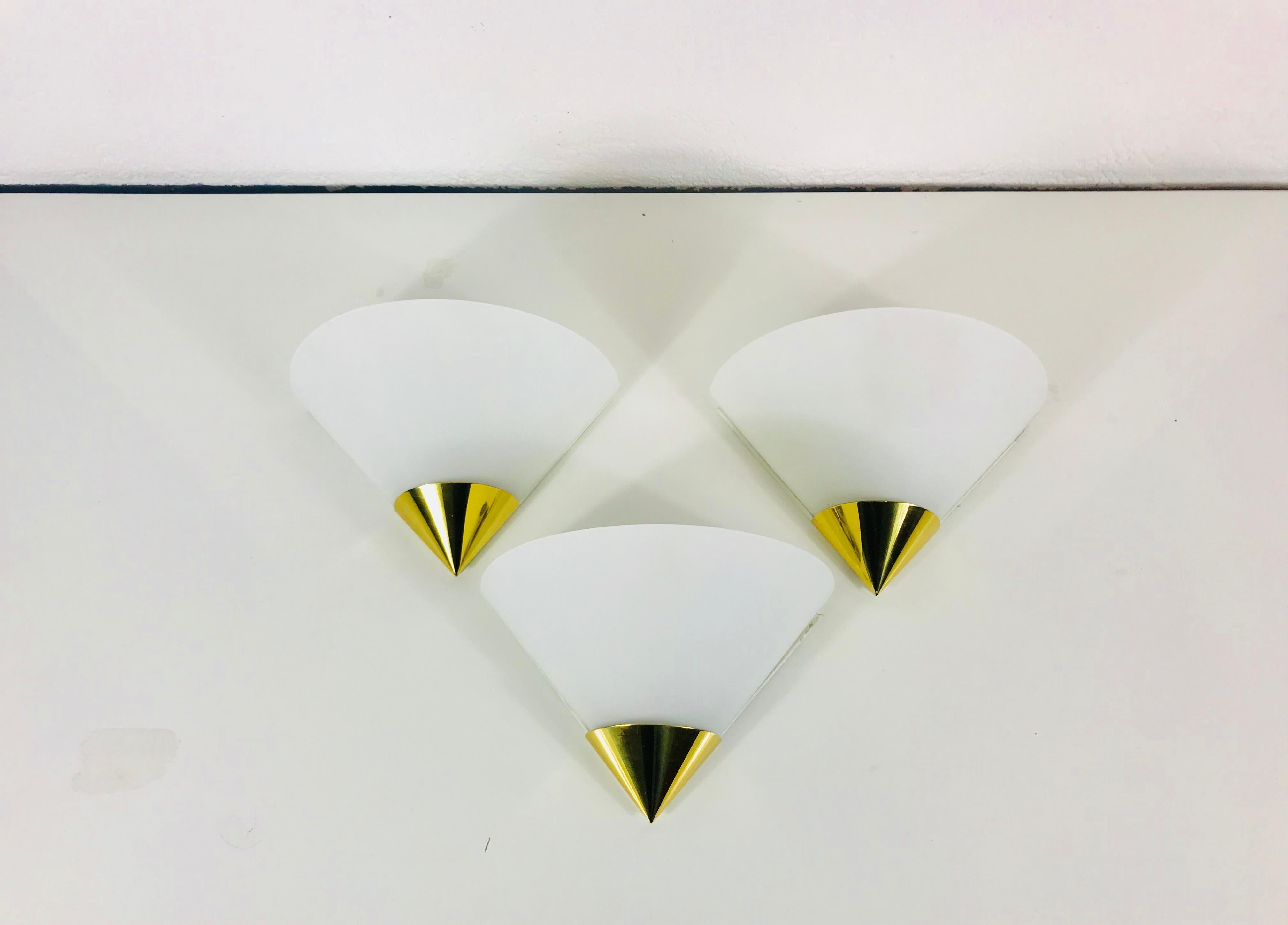 A beautiful set of 3 Mid-Century Modern wall lamps by Glashütte Limburg made in Germany in the 1970s. They have a beautiful triangle shape and are made of brass and opaline glass. The back is metal.

The light requires one E14 light bulb.