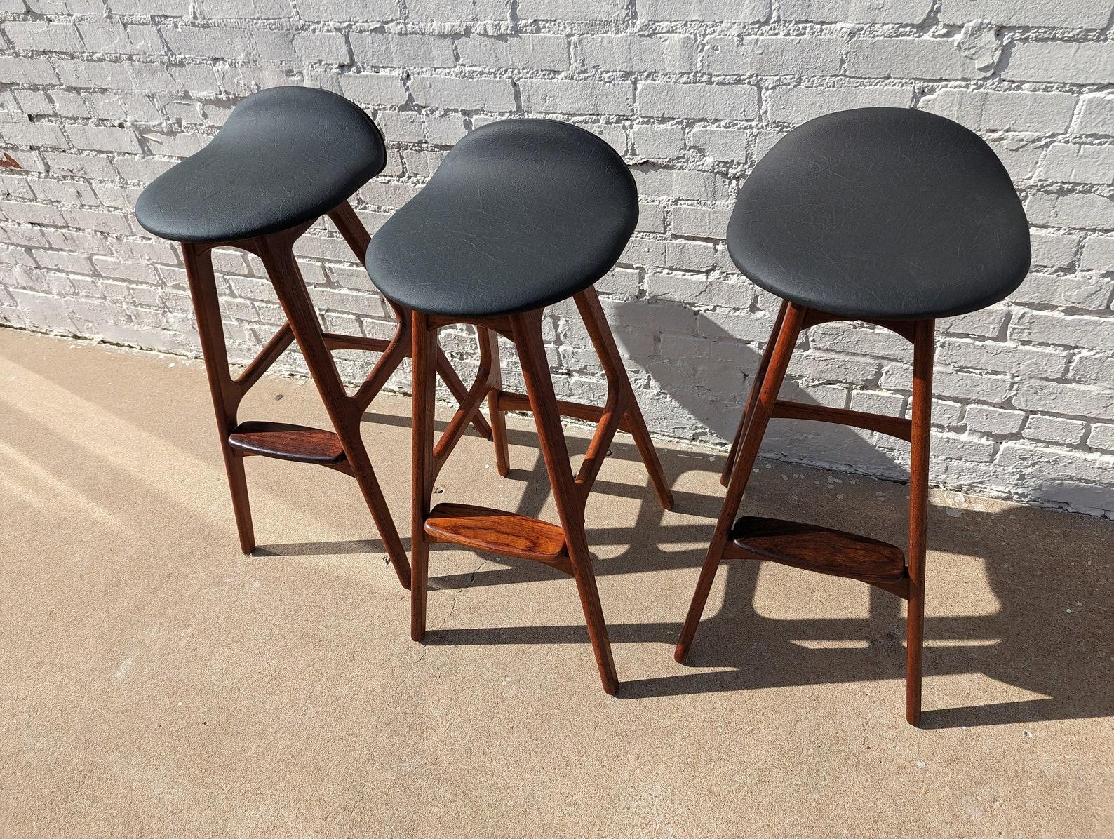Set of 3 Mid Century Danish Modern Eric Buch Teak Barstools
 
Sold as set of 3. Above average vintage condition and structurally sound. Has some expected slight finish wear and scratching on frames. Imitation leather seats are new. One stool has an