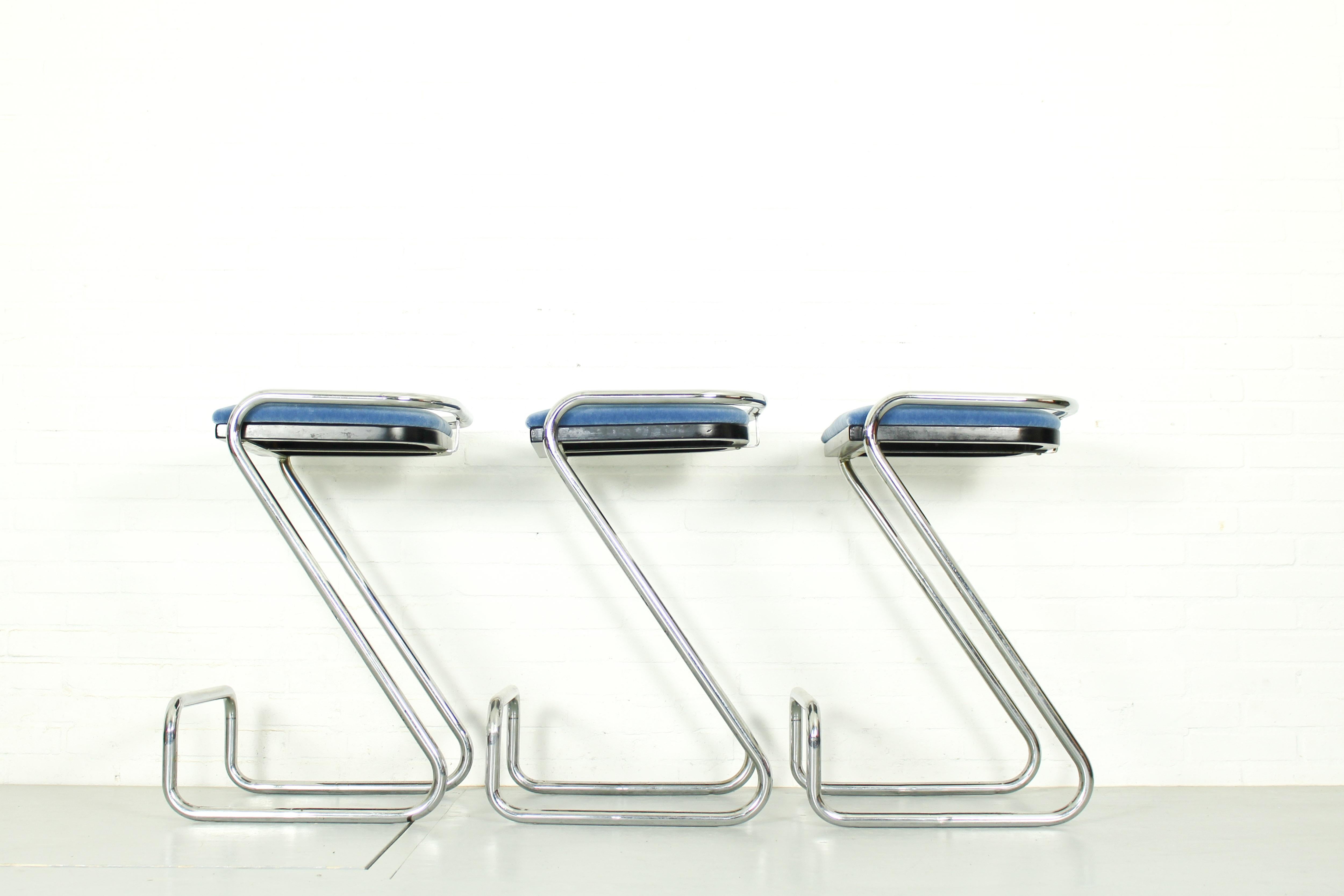 In the style of Charlotte Perriand, a set of 3 Minimalist chromed steel tube bar stools. Z form with elevated footrest rail. Lightblue mohair fabric upholstered seating. Signed 