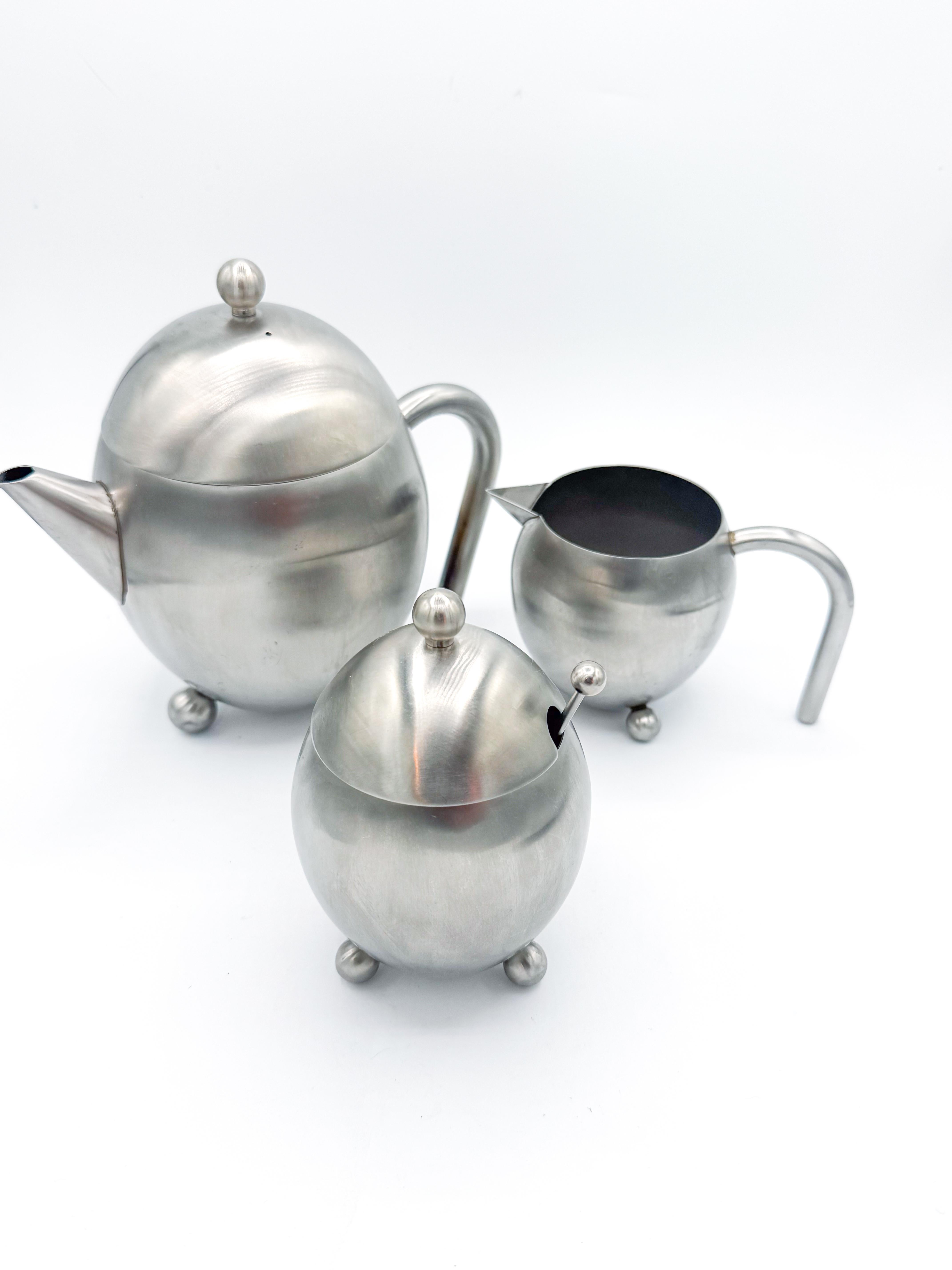 Juego de tres piezas de servicio de té de acero inoxidable cepillado con siluetas atrevidas y esculturales y juguetonas patas de bola, un ejemplo sorprendente del diseño moderno de mediados de siglo. Este raro conjunto incluye una tetera, una