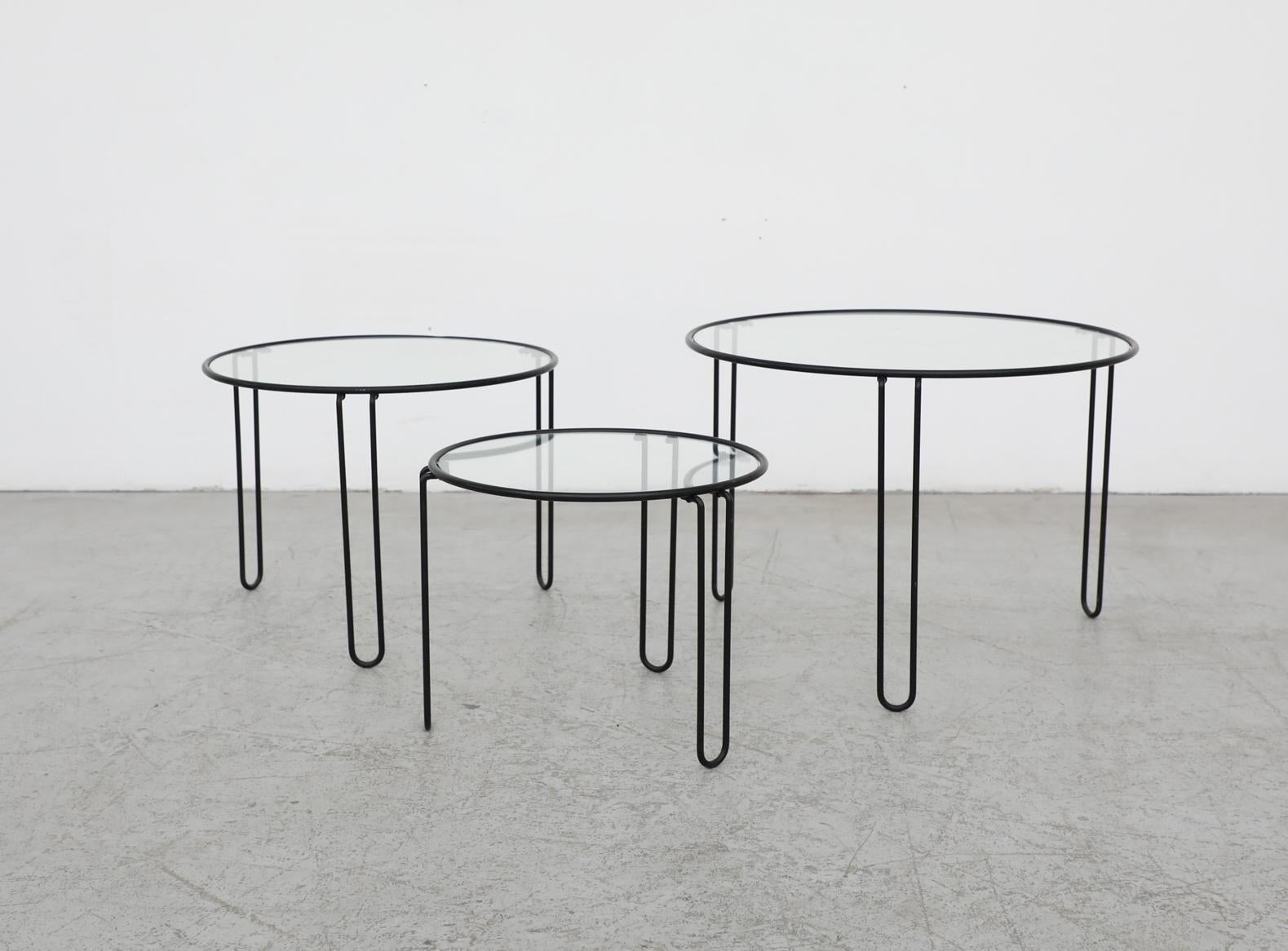 Mid-Century MOD Satz von 3 schwarz emailliertem Metall minimalistische runde Draht Verschachtelung Tabellen. Jeder Tisch hat drei abgerundete, U-förmige Beine und eingelassene Glasplatten. In Originalzustand mit sichtbaren Verschleiß einschließlich
