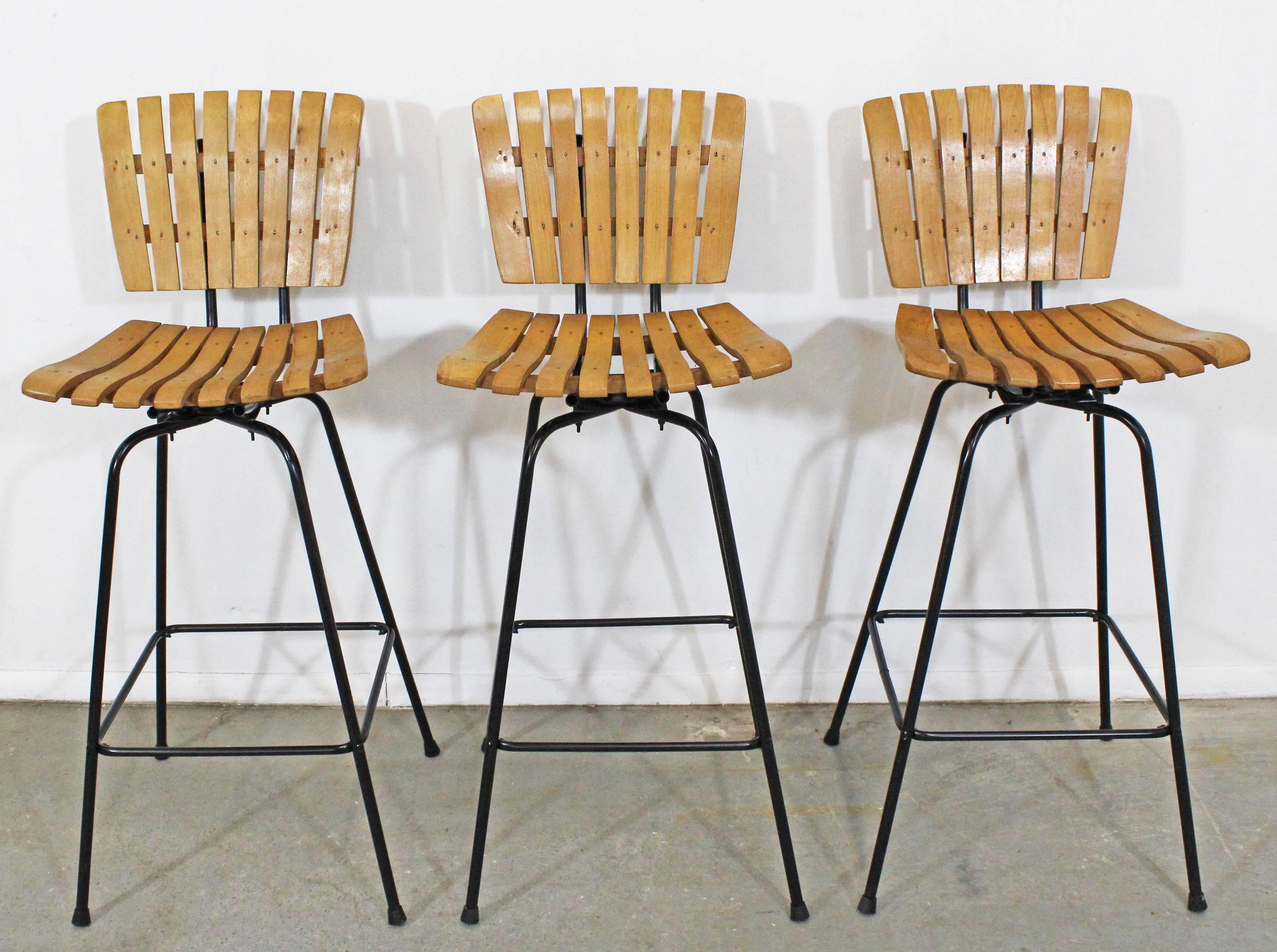 Offered is a set of 3 Umanoff style slat bar stools that swivel. The stools are in good condition for their age, showing some wear (see photos) with repainted bases and new foot cups. They are not signed.

Approximate dimensions:
17