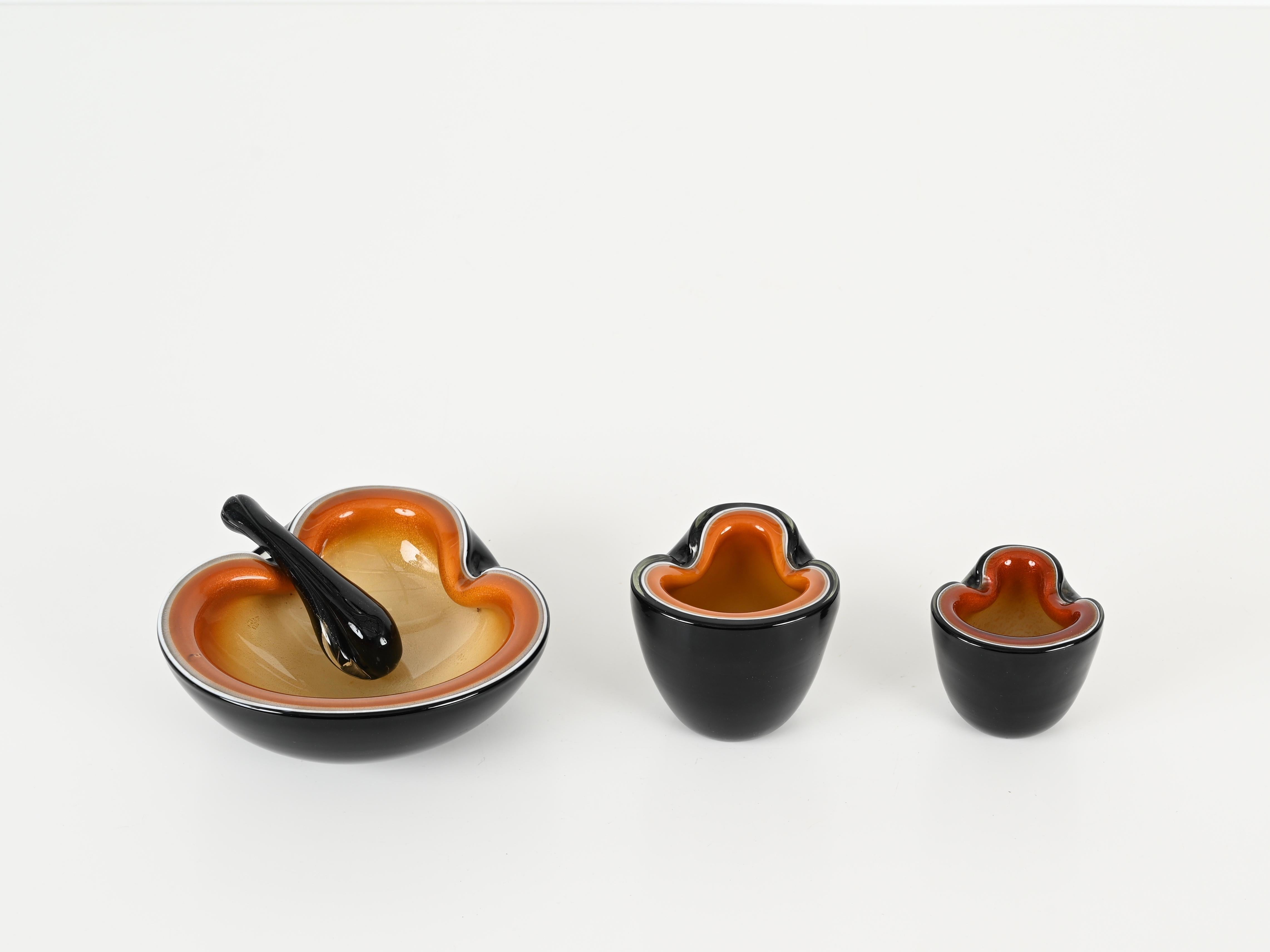 Wonderful Mid-Century collection of three decorative bowls or ashtrays in sommerso Murano mouth blown black, orange and white glass with gold details. This incredibly charming and unique set was produced in Murano, Italy during the 1970s.

In