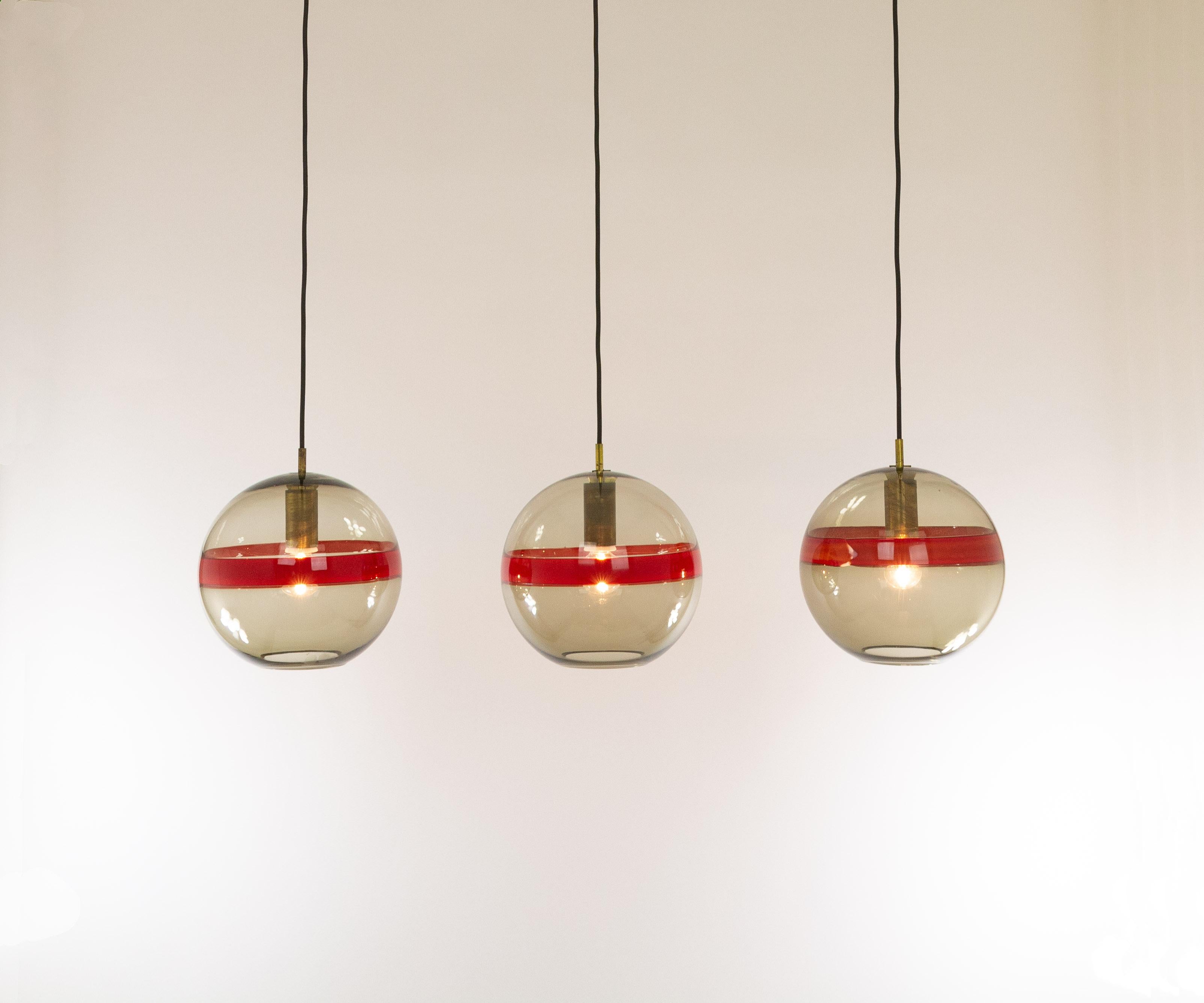 Set of three Murano glass pendants model 5199 by Ludovico Diaz de Santillana for Venini, produced in the 1960s.

The lamps are made of smoked glass with a red band in the middle. They are handmade and therefore the color of the band is not