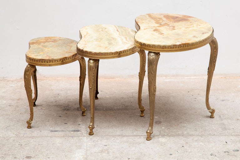 Set of three Hollywood Regency style nesting tables. Kidney shaped solid marble tops rest on three sculptural brass legs.
The nesting tables are in very good condition.

Measurements:
Large
57 W x 44 H x 34 D cm 
Med
47 W x 40 H x 28 D cm