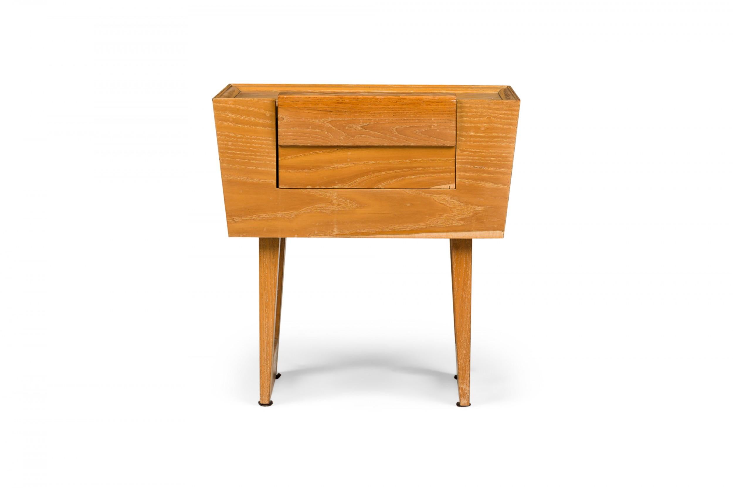 SET of 3 American mid-century wooden nightstands with a slightly cerused finish, tapered trapezoidal cabinets containing a single drawer, resting on two bracket-shaped legs. (PAUL LASZLO FOR BROWN SALTMAN)(PRICED AS SET)