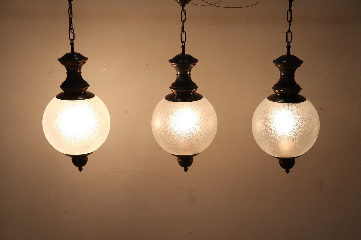 We present this particular set of three pendant lamps, Italian production circa 1960s. The lamps have a patinated brass structure and glass bowl. 

These lamps, despite not having any brands or signatures, have quality in materials and design. These