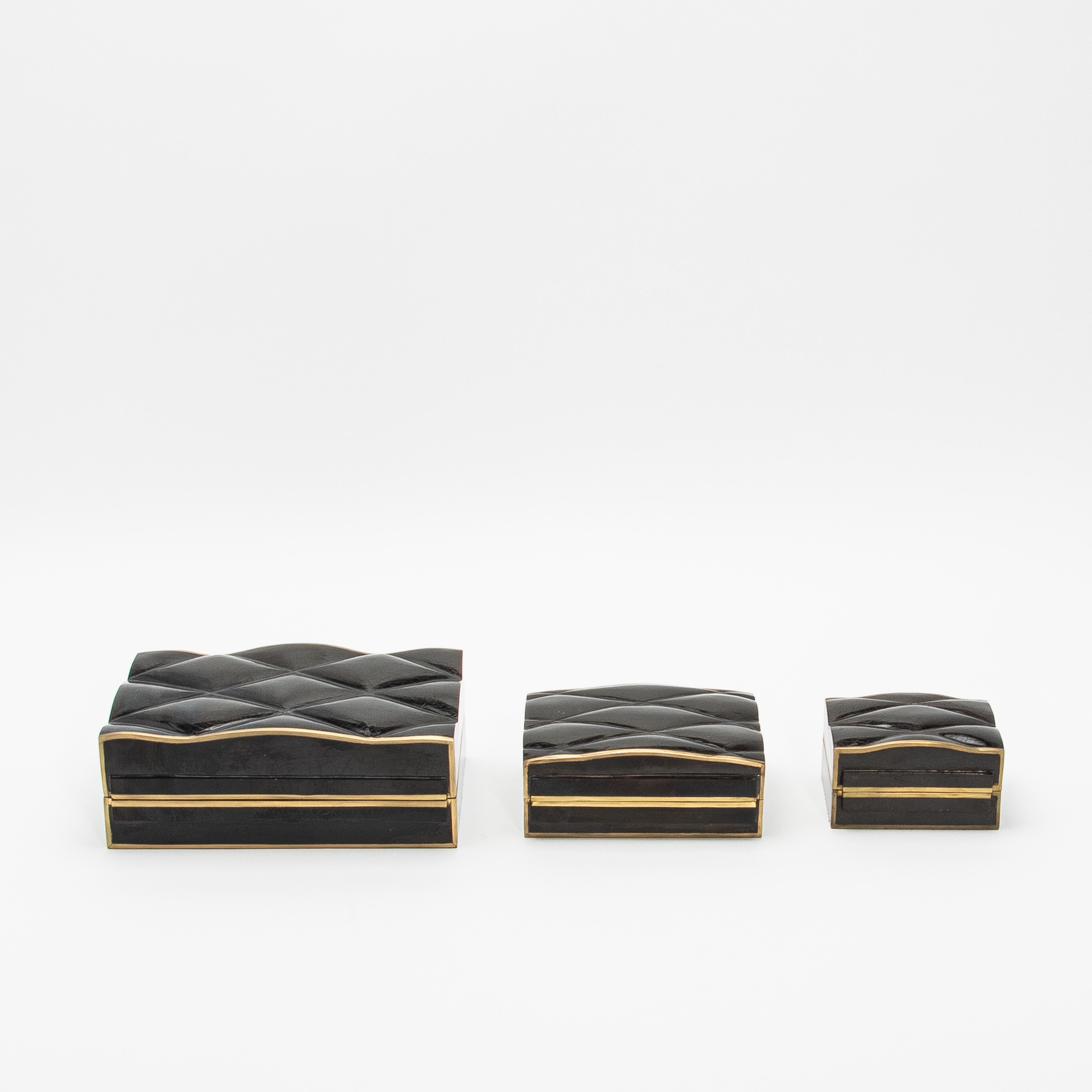 The Coco box collection by Kifu Paris exemplifies luxury through its intricate design and meticulous craftsmanship. This set of three quilted boxes in black pen shell, framed with a bronze patina brass edge, radiates elegance and sophistication. The