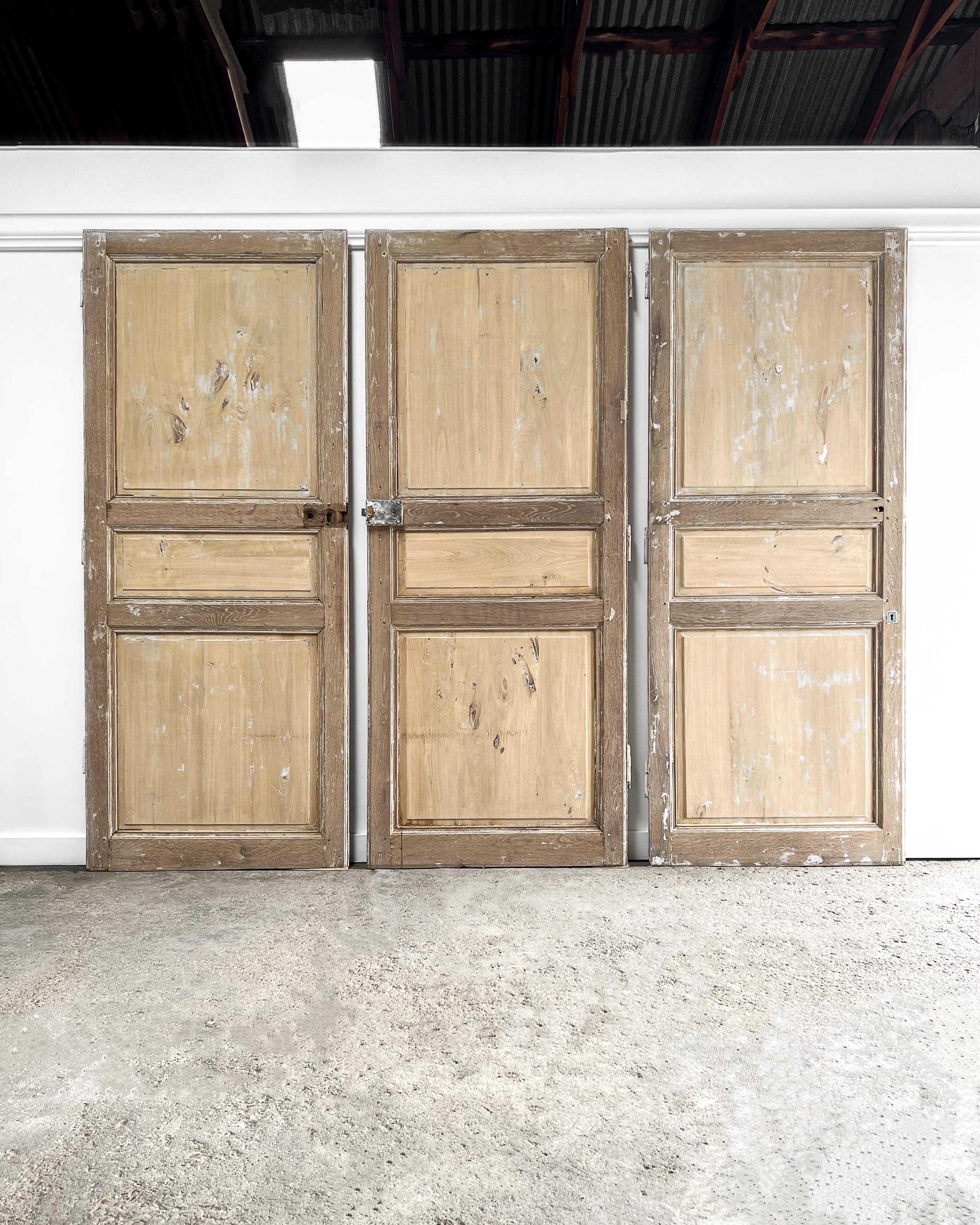 A set of three interior doors reclaimed from a home in the French countryside. Hand-crafted from poplar and oak, the doors feature a 3-panel configuration with raised panels and beveled details. Install these in your home to add an authentic air of