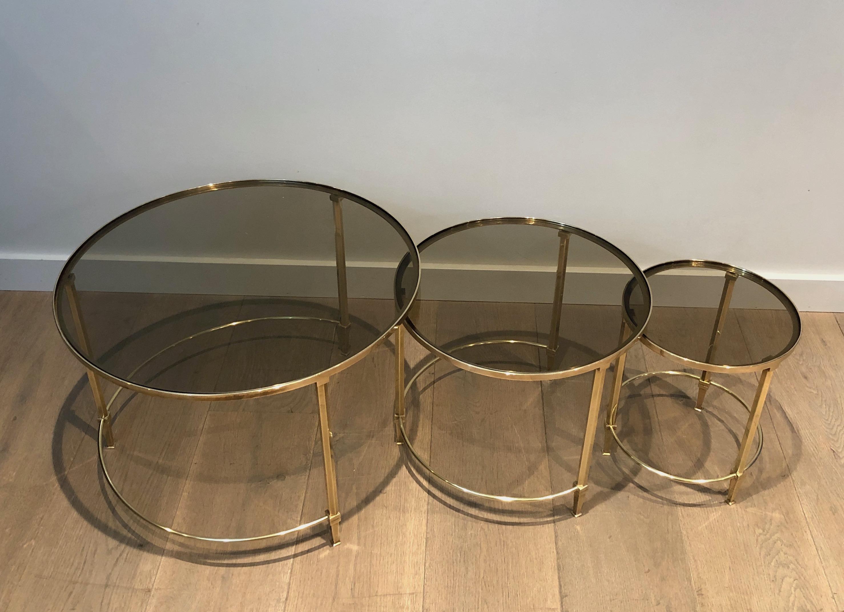 This set of 3 round nesting tables is made of brass with smoked glass. This is a French work by famous designer Maison Ramsay. Circa 1940.